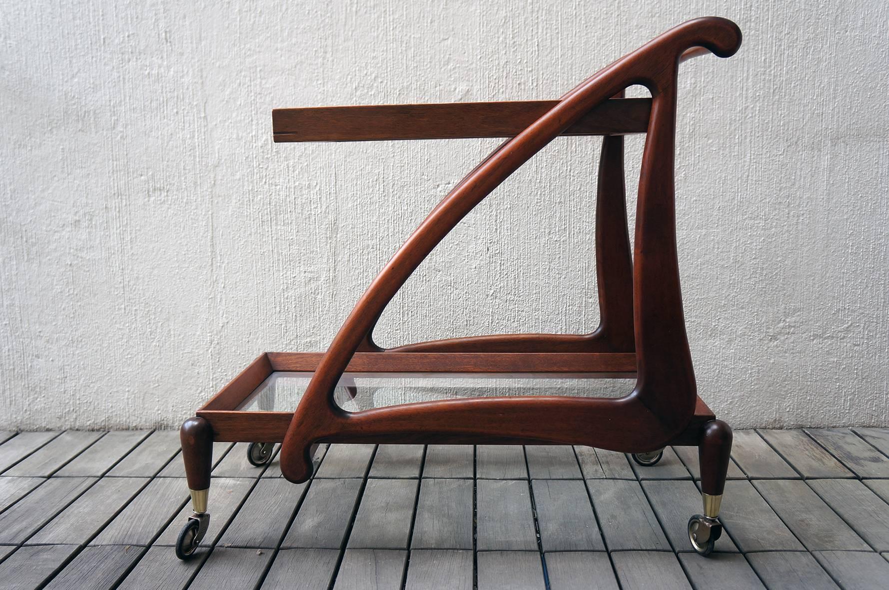 Mexican Modernist bar trolley or serving cart, made of mahogany wood, with two rectangular glass shelves and a wooden frame.