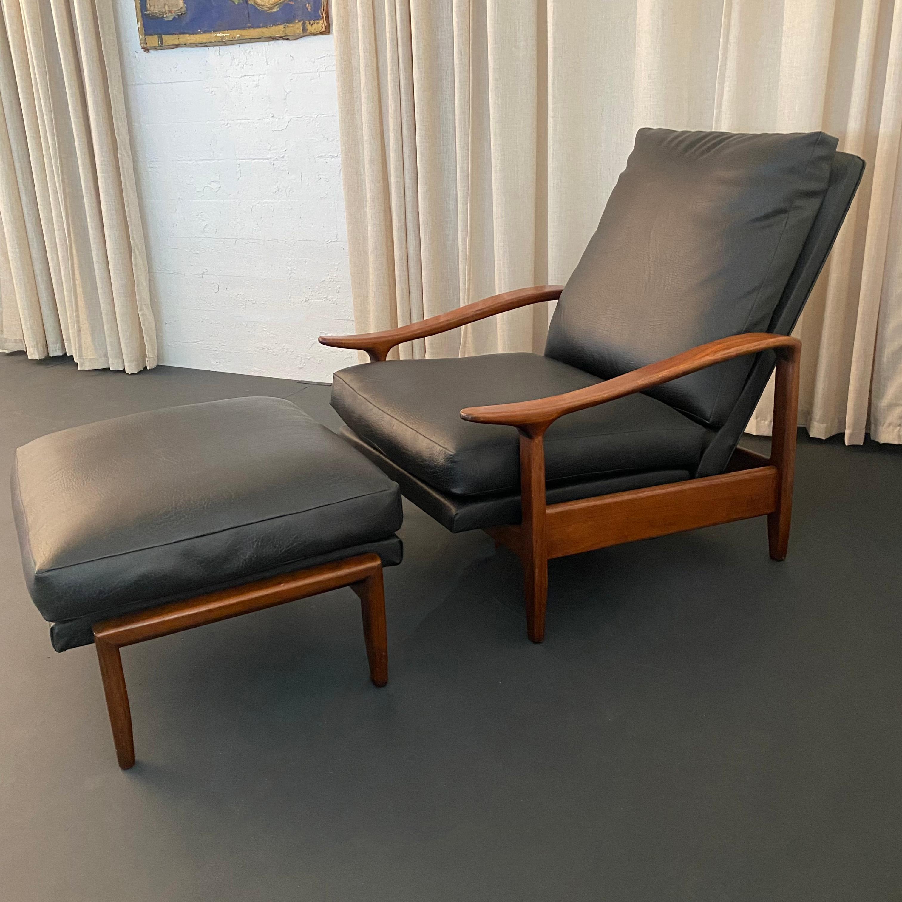 This Mid-Century Modern recliner lounge chair and matching ottoman set are attributed to Milo Baughman. The set features charcoal black leather upholstery that contrasts nicely with the medium toned walnut frame. The contoured arms really set this