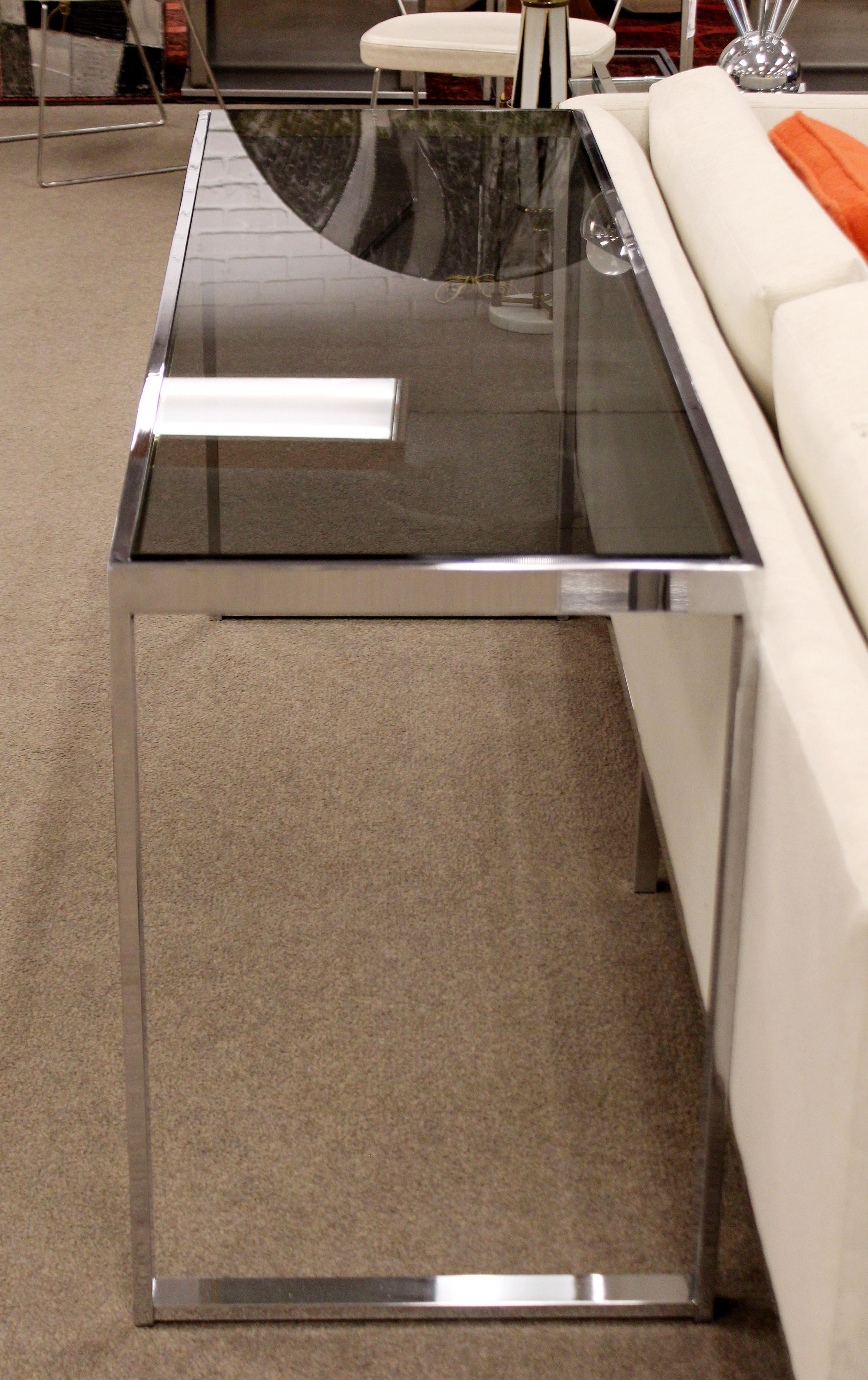 For your consideration is a simple and chic console table, with smoked glass on a flat bar chrome base, by Milo Baughman, circa 1970s. In excellent condition. The dimensions are 60