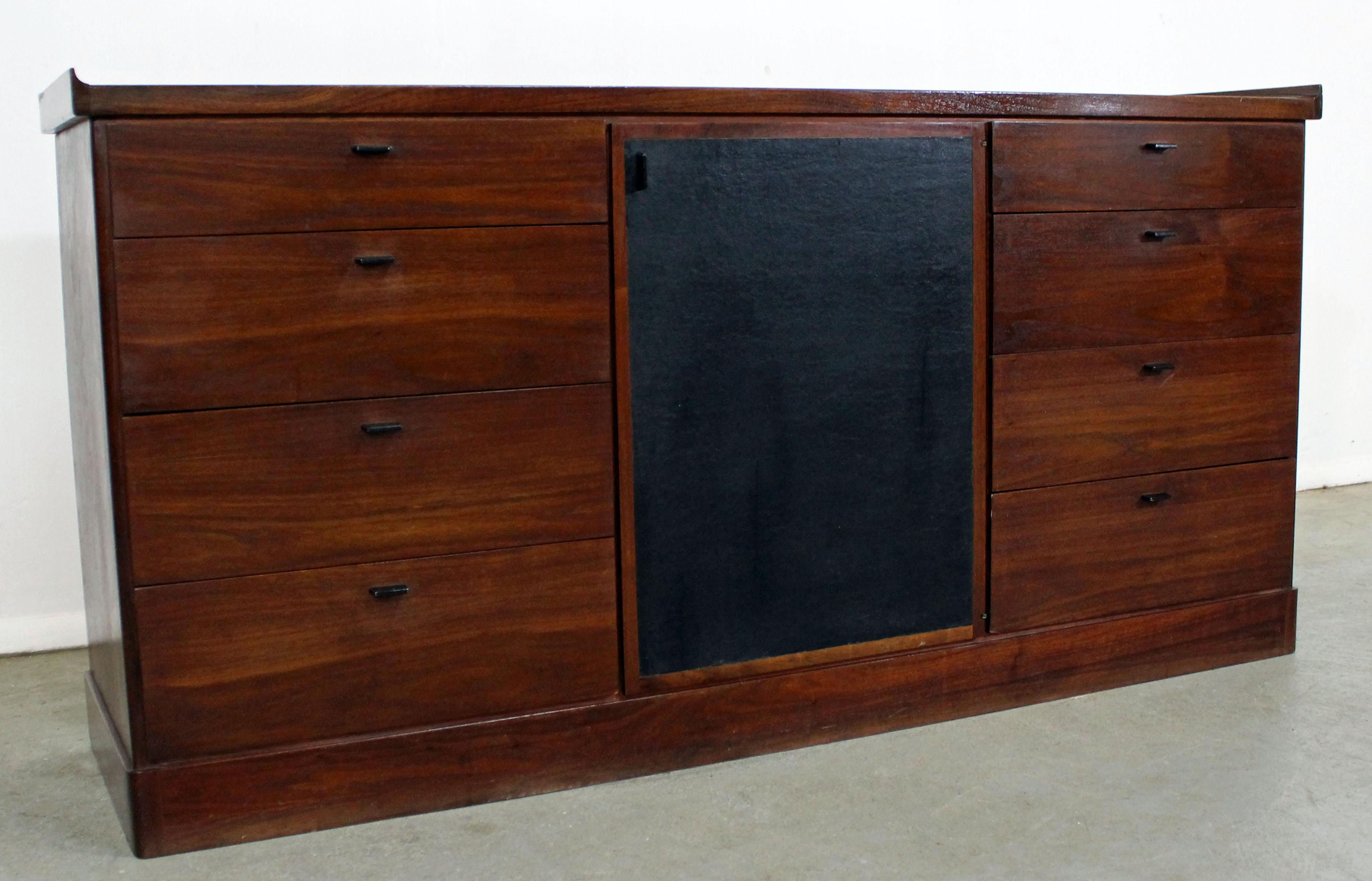Offered is a Mid-Century Modern walnut credenza. Features flared edges, 12 drawers altogether, with 4 hidden behind a black door. Can be used as a dresser, sideboard, or credenza. It is in very good condition for its age, shows some age wear