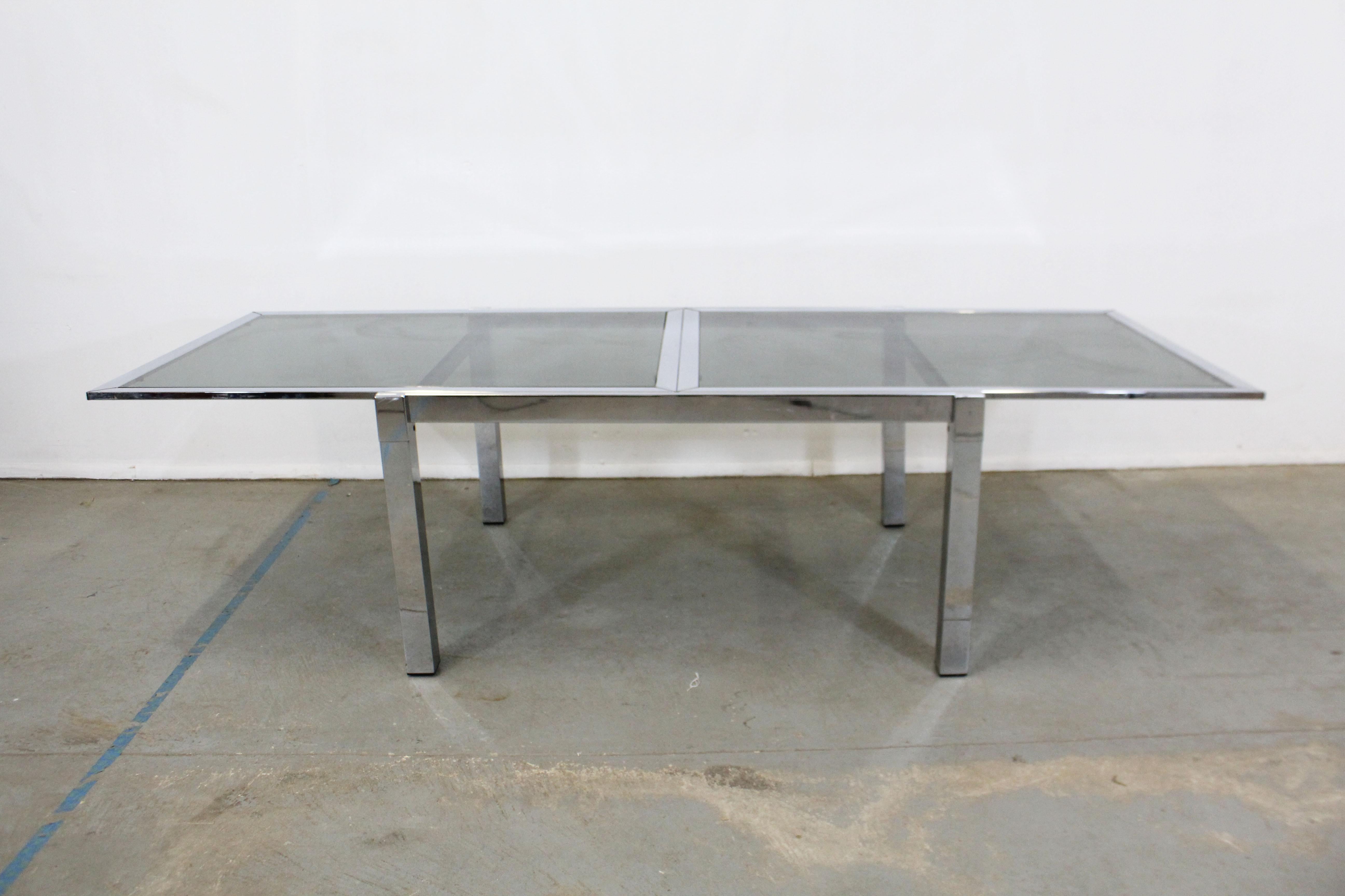 Offered is a DIA vintage Mid-Century Modern dining table. This table is made of chrome and has a smoky black glass top as well as an extension board underneath the top. The bottom pulls out to extend. It is in good condition with some light surface