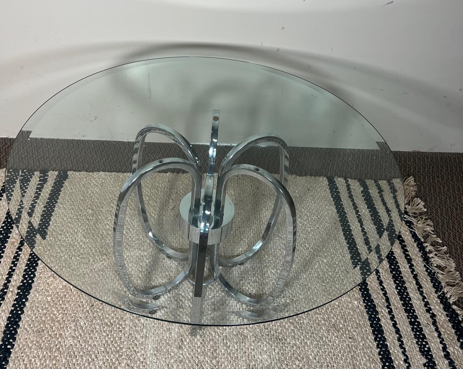 This is a beautiful round chrome and glass coffee table.. Attributed to Milo Baughman. Very good condition. No chips on glass. Some wear on the chrome base. One of the felt covers on the feet missing. Most of the rubber plugs on the top that the