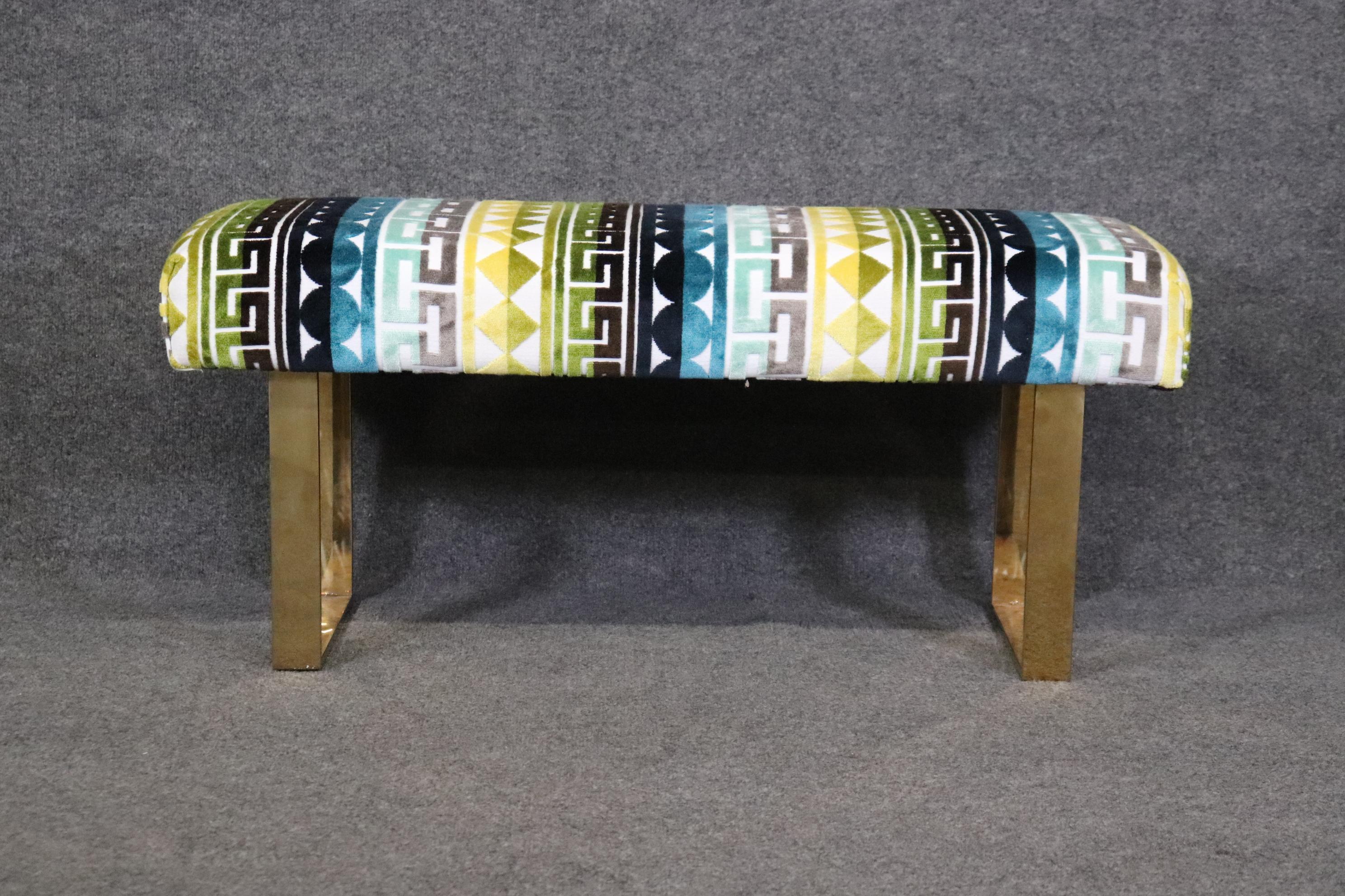 This is a gorgeous brass and abstract upholstered Milo Baughman style bench. The bench is newly upholstered in a bright and colorful abstract fabric and is in excellent overall condition. The bench measures 40.25 wide x 16.5 deep x 17.75 tall and