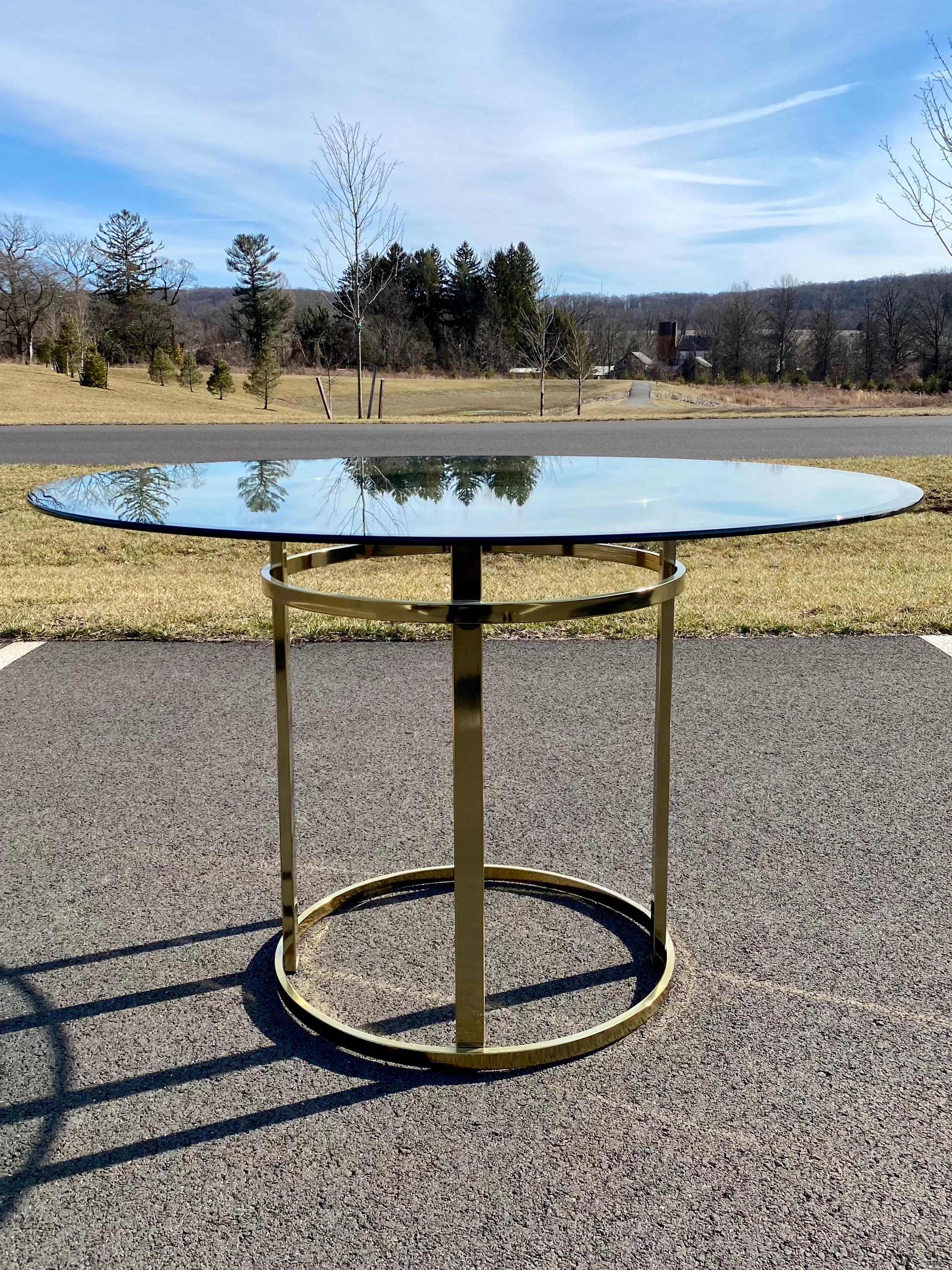 Mid-Century Modern brass and glass round dining or center hall table. Sleek style of Milo Baughman circa 1970s-1980s. This sculptural table features a shiny brass gold tone metal base with thick 1/2 inch round beveled glass