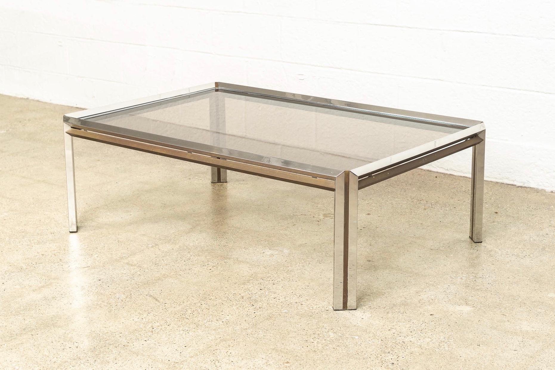 This vintage Mid-Century Modern chrome, brass and glass rectangular coffee table in the style of Milo Baughman is circa 1970. The unique design features a faceted chrome frame accented by solid brass side bars and inlaid brass striped legs. The