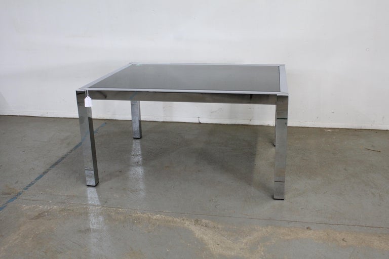 Offered is a vintage Mid-Century Modern Milo Baughman style dining table. This table is made of chrome and has a smoky black glass top as well as an extension board underneath the top. The bottom pulls out to extend. It is in good condition with