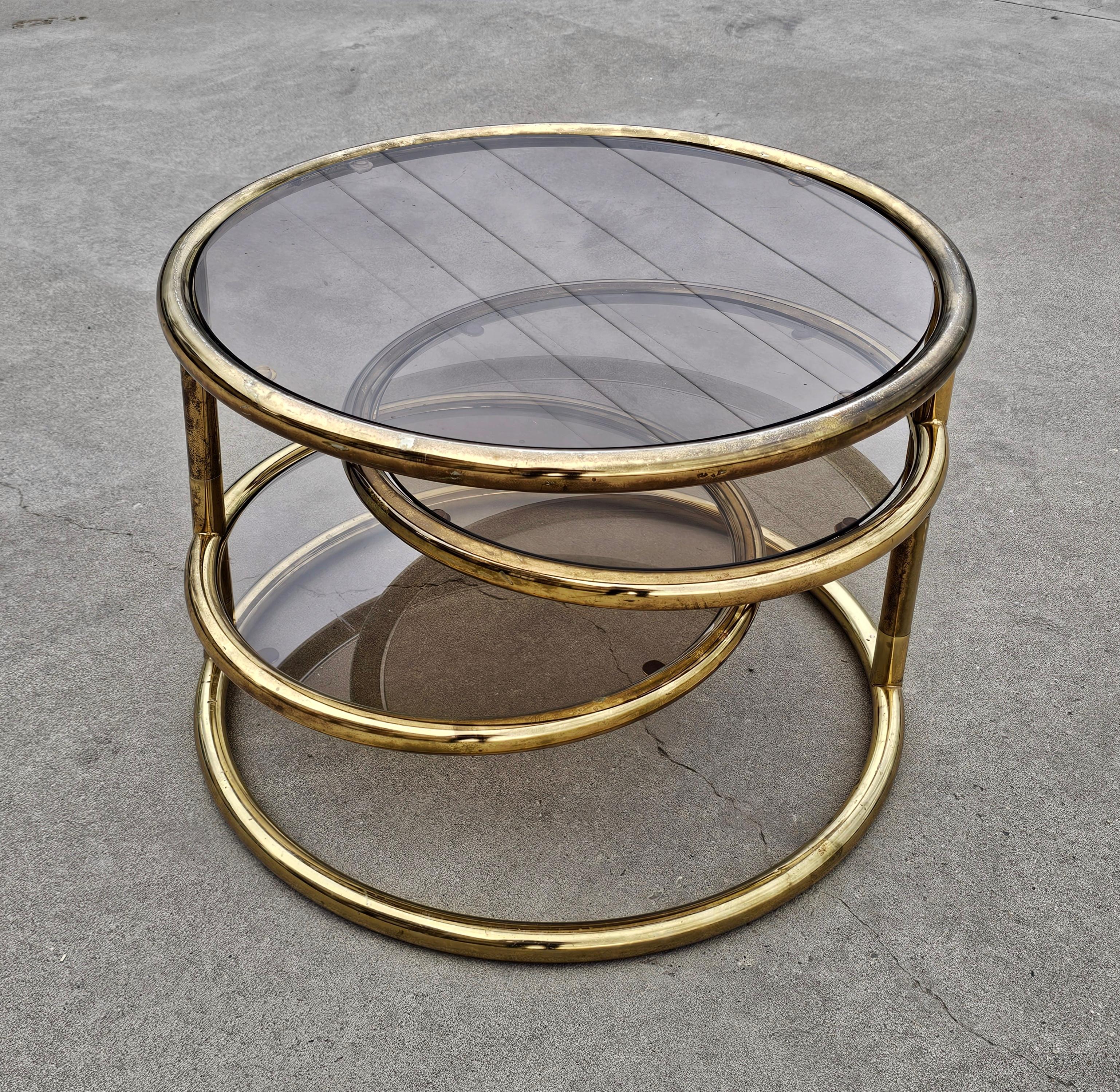 In this listing you will find a stunning Mid Century Modern swivel coffee table that many attribute to Milo Baughman. It is done in brass plated steel, which many mix with brass. Table features three circular tops done in smoked glass out of which