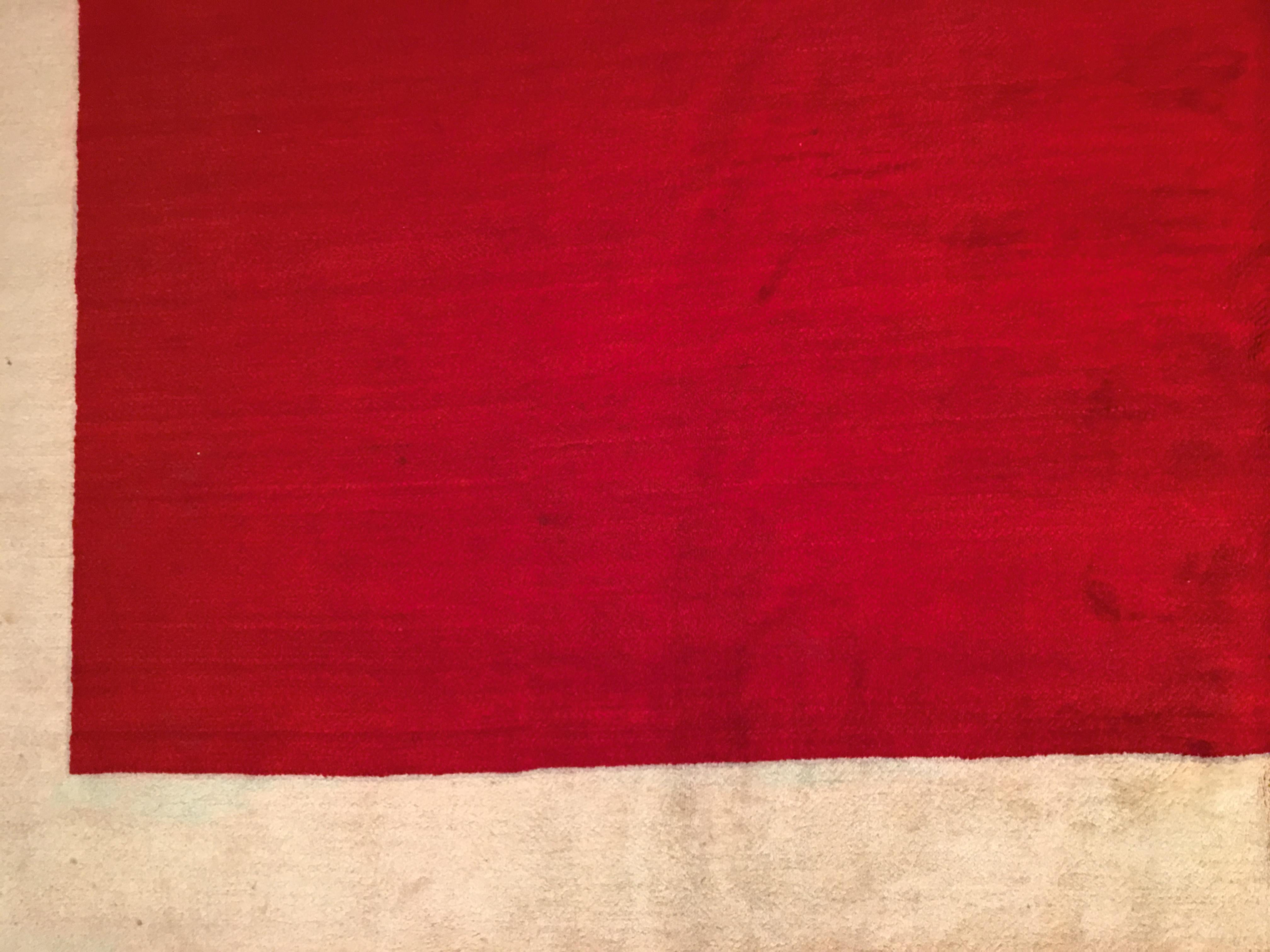 Un tappeto indiano modernista di grande impatto visivo, caratterizzato da un campo aperto rosso brillante, incorniciato da un ampio bordo avorio a contrasto. Firmato dall'Atelier A sulla striscia di guardia esterna in alto a destra e con il