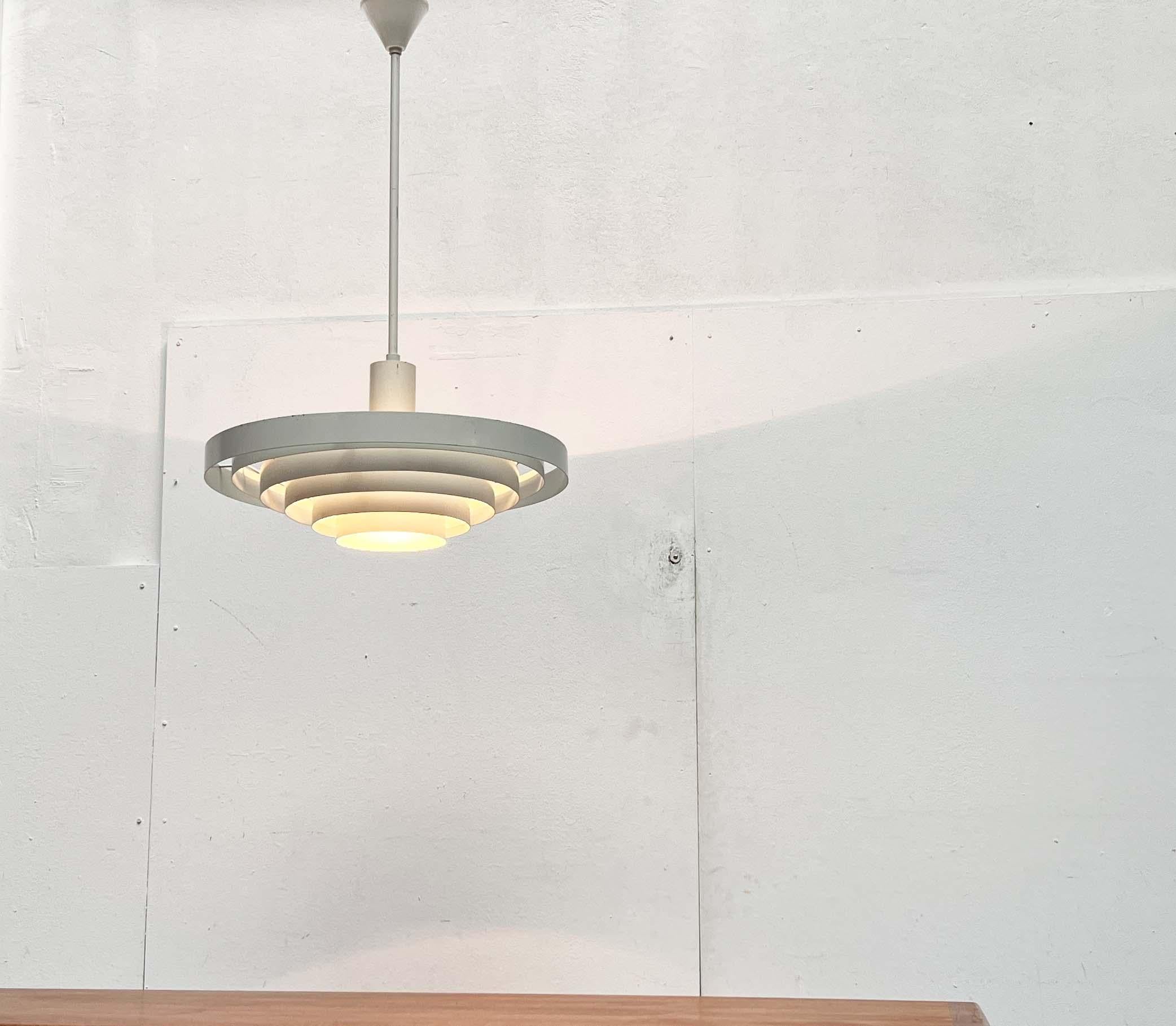 Lampada a sospensione a stelo minimalista dell'azienda tradizionale finlandese Idman. Il disegno è attribuito a Paavo Tynell.

Un design funzionale. Il corpo della lampada è costituito da lamelle ad anello in metallo laccato bianco. Questi sono