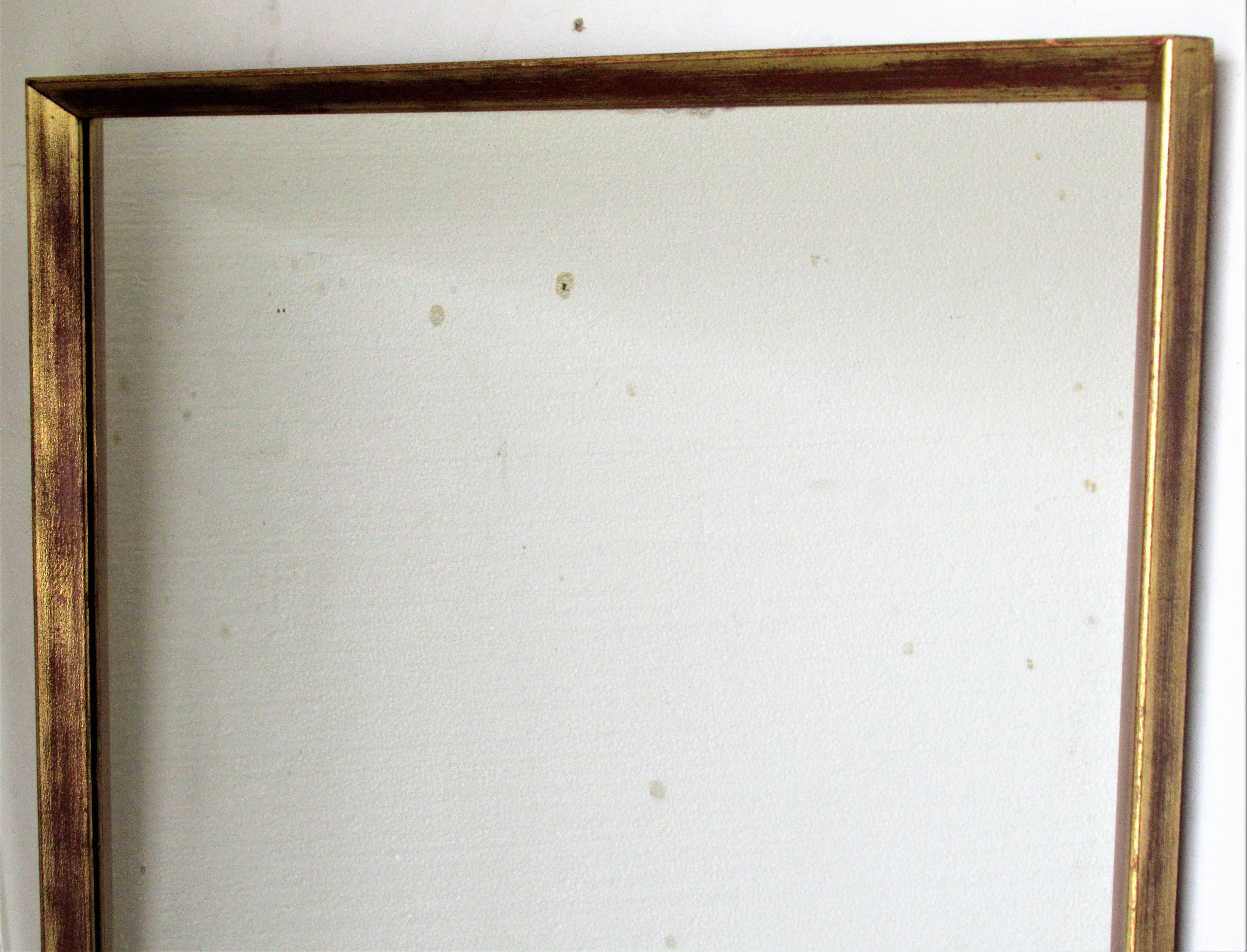  Miroir mural rectangulaire minimaliste encadré en bois doré avec une surface dorée d'origine magnifiquement vieillie et des reflets de bole rouge. Le verre miroir d'époque est brillant avec des zones de petites taches d'oxydation. Probablement