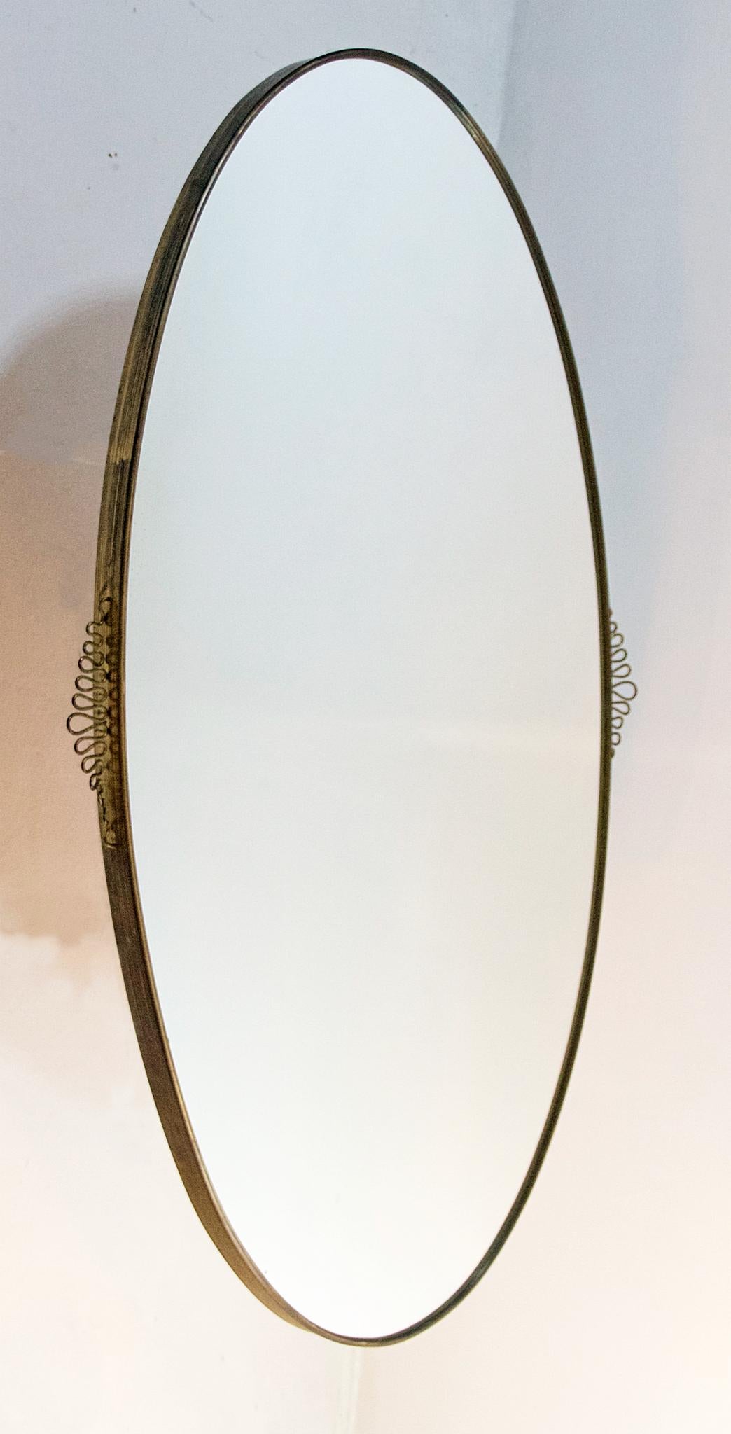 An oval mirror in the manner of Gio Ponti from the 1950s in brass and with brass ornaments significant for the era on the side.