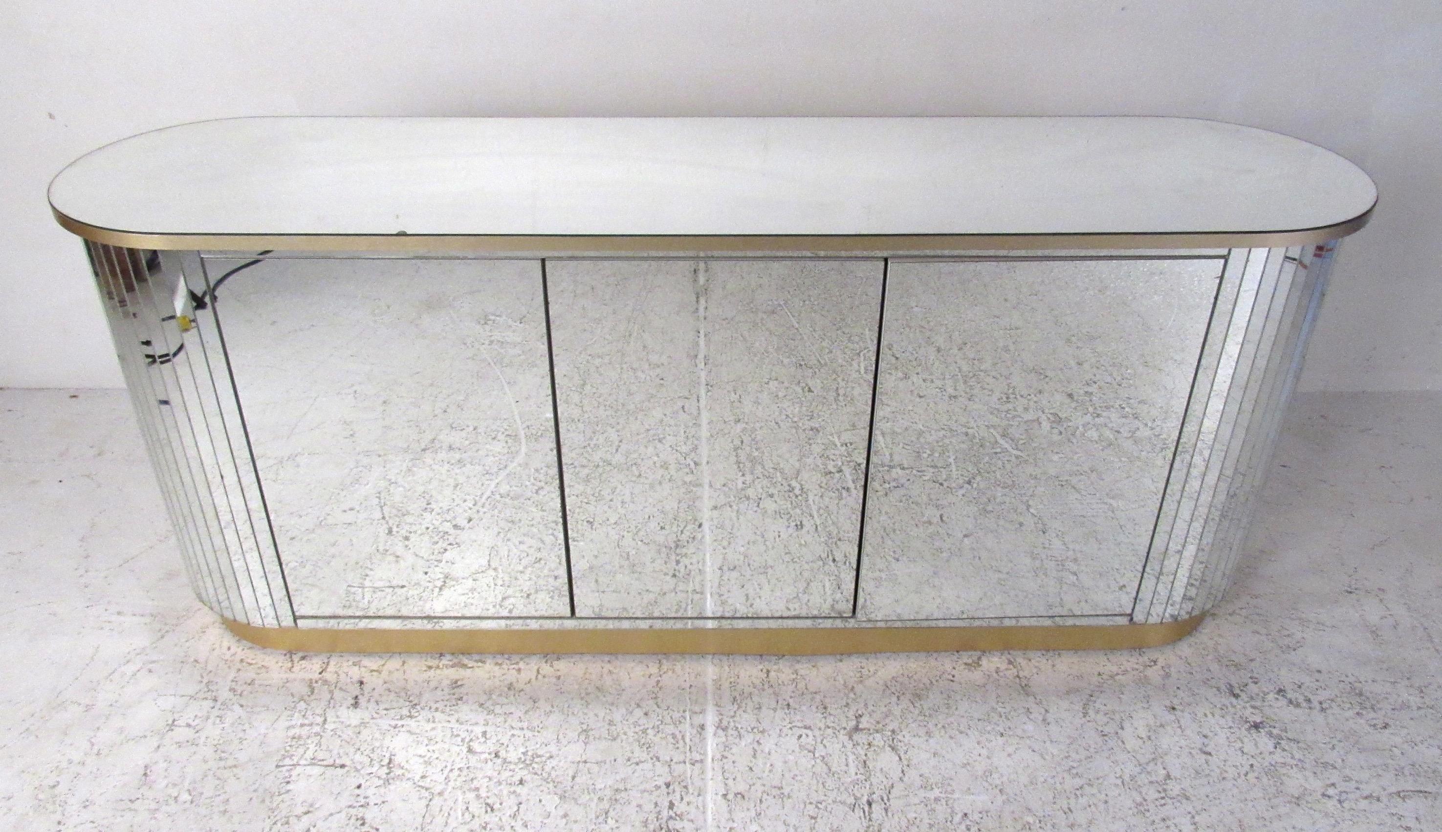 Mid-Century Modern mirrored three-door credenza with rounded sides and gold metal accent trim. The round sides are covered in mirrored strips creating a dramatic, faceted appearance. The white laminate interior features two adjustable shelves and