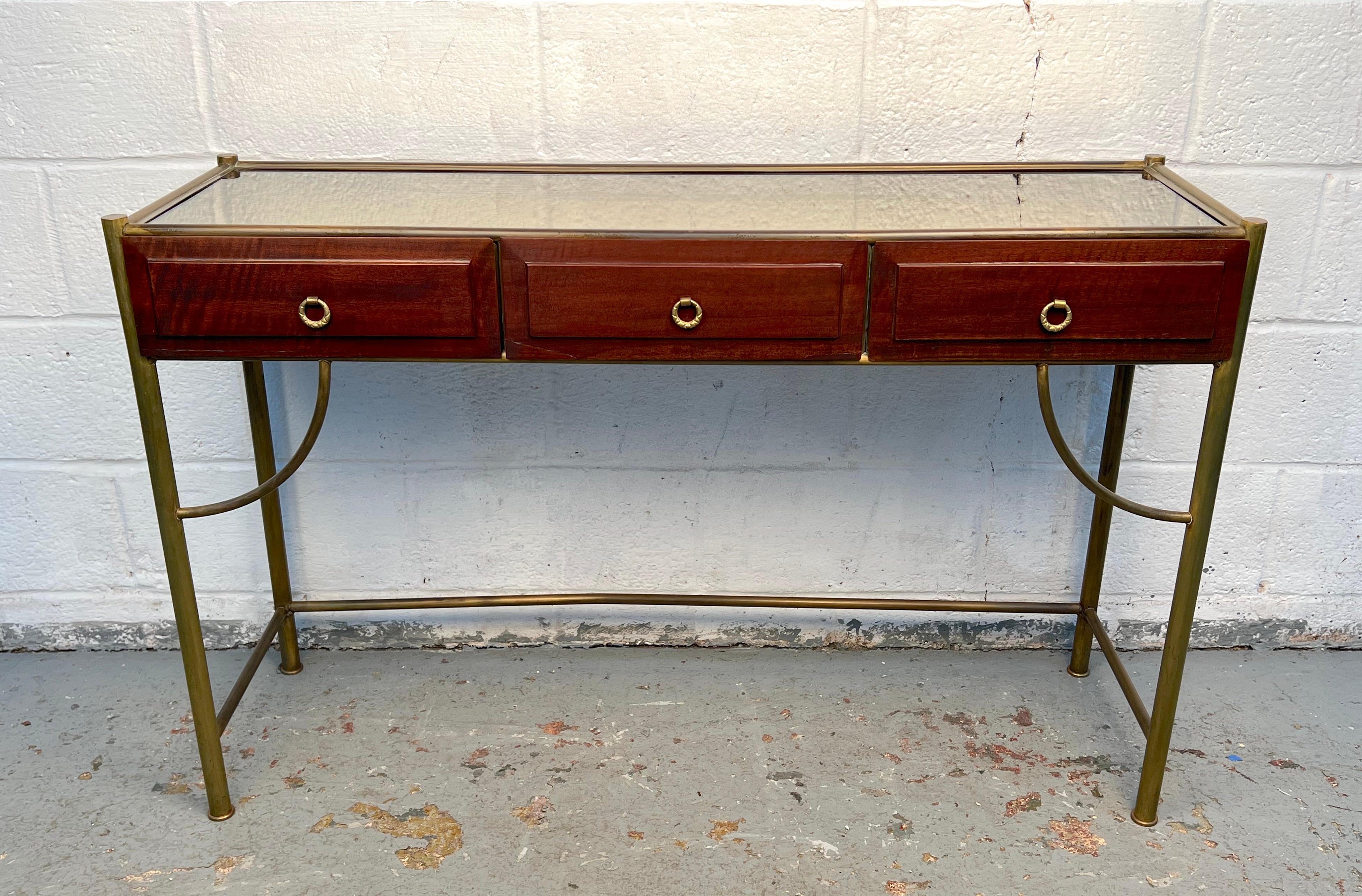 Elegante consola de mediados de siglo con tapa de espejo enmarcada con un ribete de latón. Su forma aerodinámica y su superficie reflectante crean una presencia sofisticada, perfecta para usar en una entrada, un pasillo o un salón. Una pieza