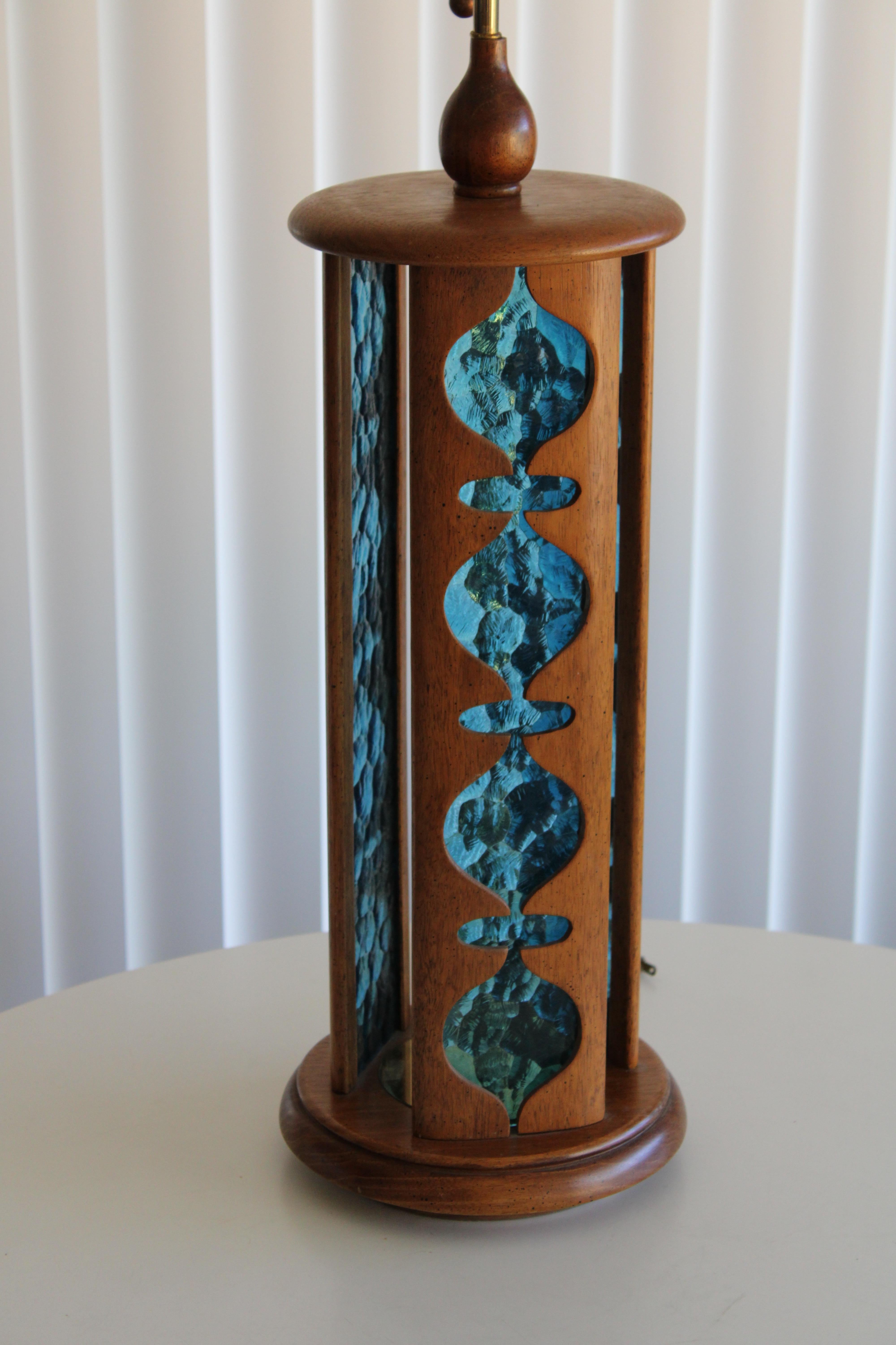 A tall mid century table lamp by Modeline. Three solid walnut panels have modern shaped cut-outs, and behind is bright blue textured lucite. Pull-chain bakelite socket has original Modeline label. Lamp measures 41