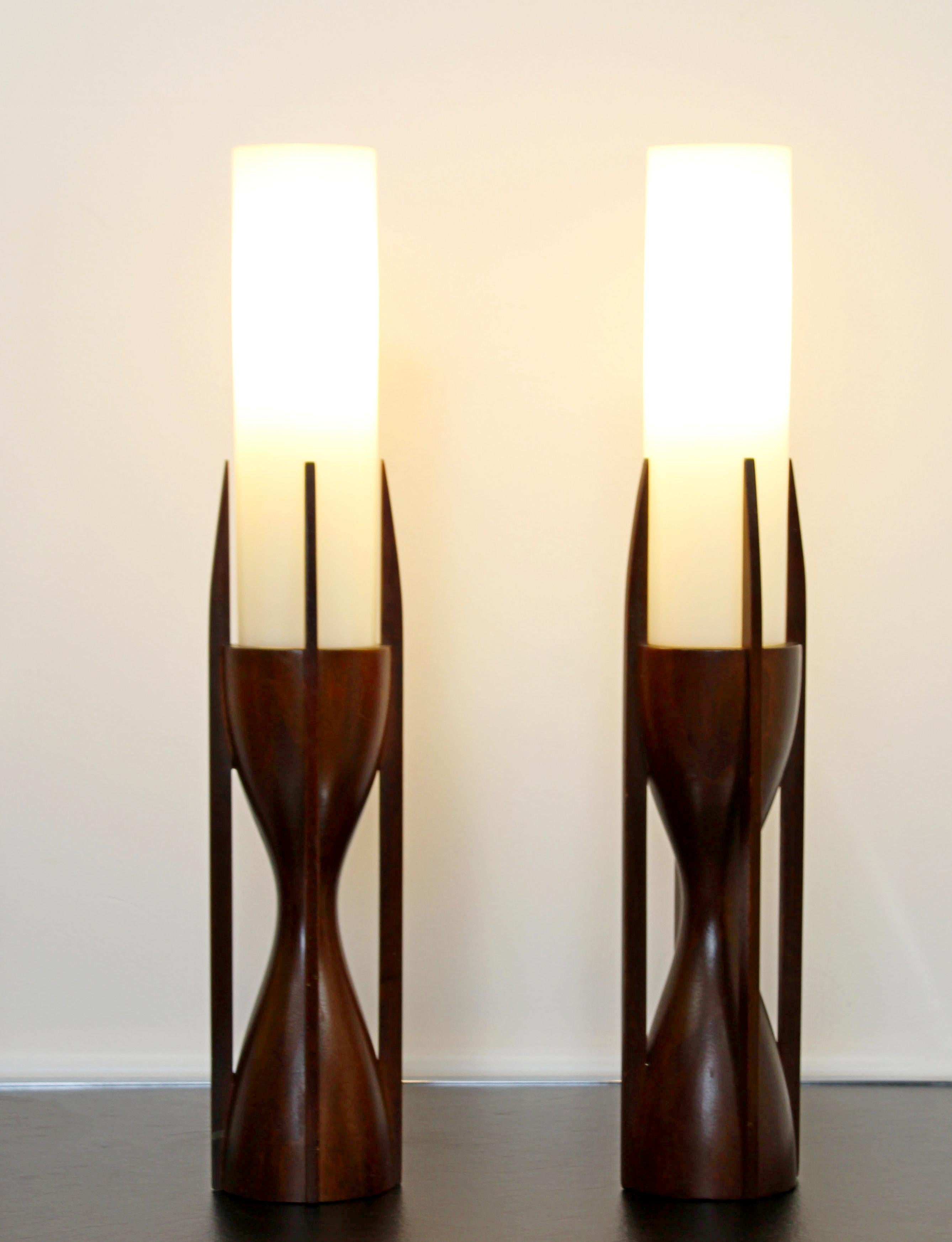 For your consideration is a gorgeous, small pair of mahogany wood and glass table lamps, in a sculptural hourglass shape, by Modeline Lamp Co, circa the 1960s. In very good condition. The dimensions are 3.5
