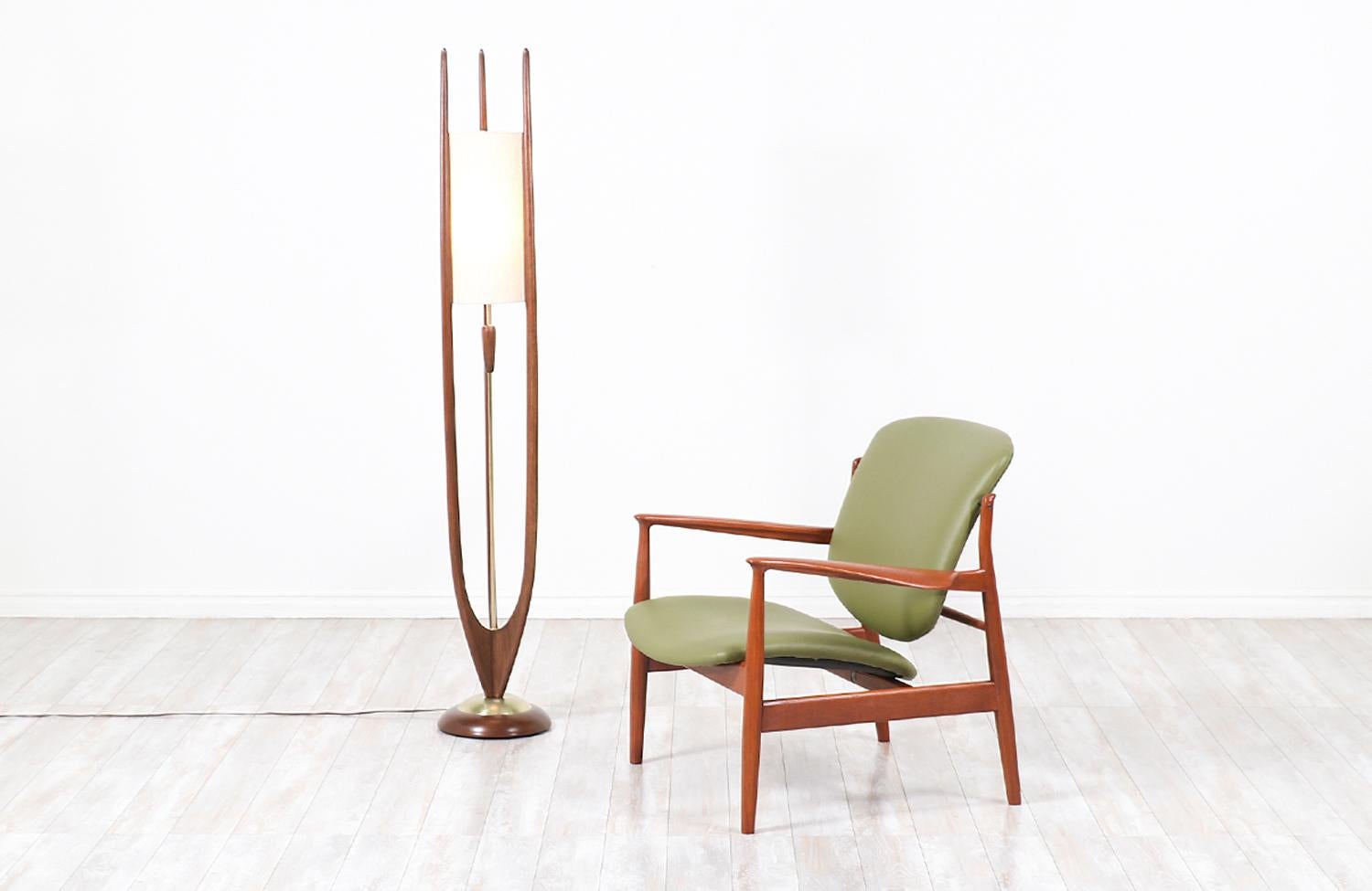 Dazzling floor lamp designed and manufactured by Modeline Lamp Co. in the United States circa 1960s. This sculptural lamp features a walnut wood frame accentuated with brass hardware and three tall prongs that support the new cylindrical linen