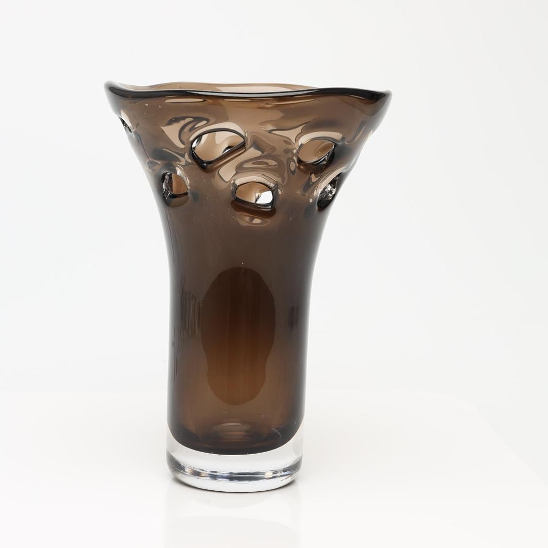 Vase aus braunem Kristall mit dekorativem Lochmuster auf dem oberen Teil. Das Design kombiniert zwei Farbblöcke - eine Trasparenz, die dem Stück ein Gefühl von Schwere verleiht.  Es wurde von Mona Morales-Schildt für Kosta Boda entworfen. Schweden,