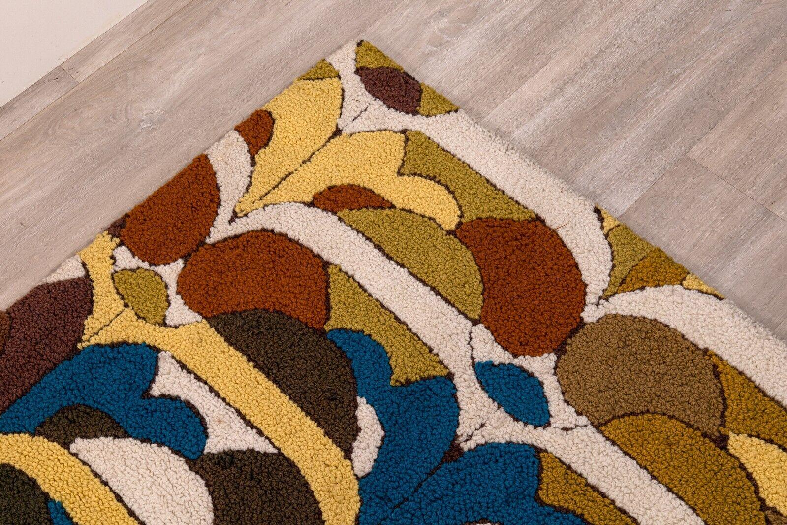 A multi colored hand made small rug artist numbered. This pretty little area rug features a colorful abstract design, with stripes and abstract shapes of different colors. This piece is filled with mostly warm, earthy colors, and is centered with