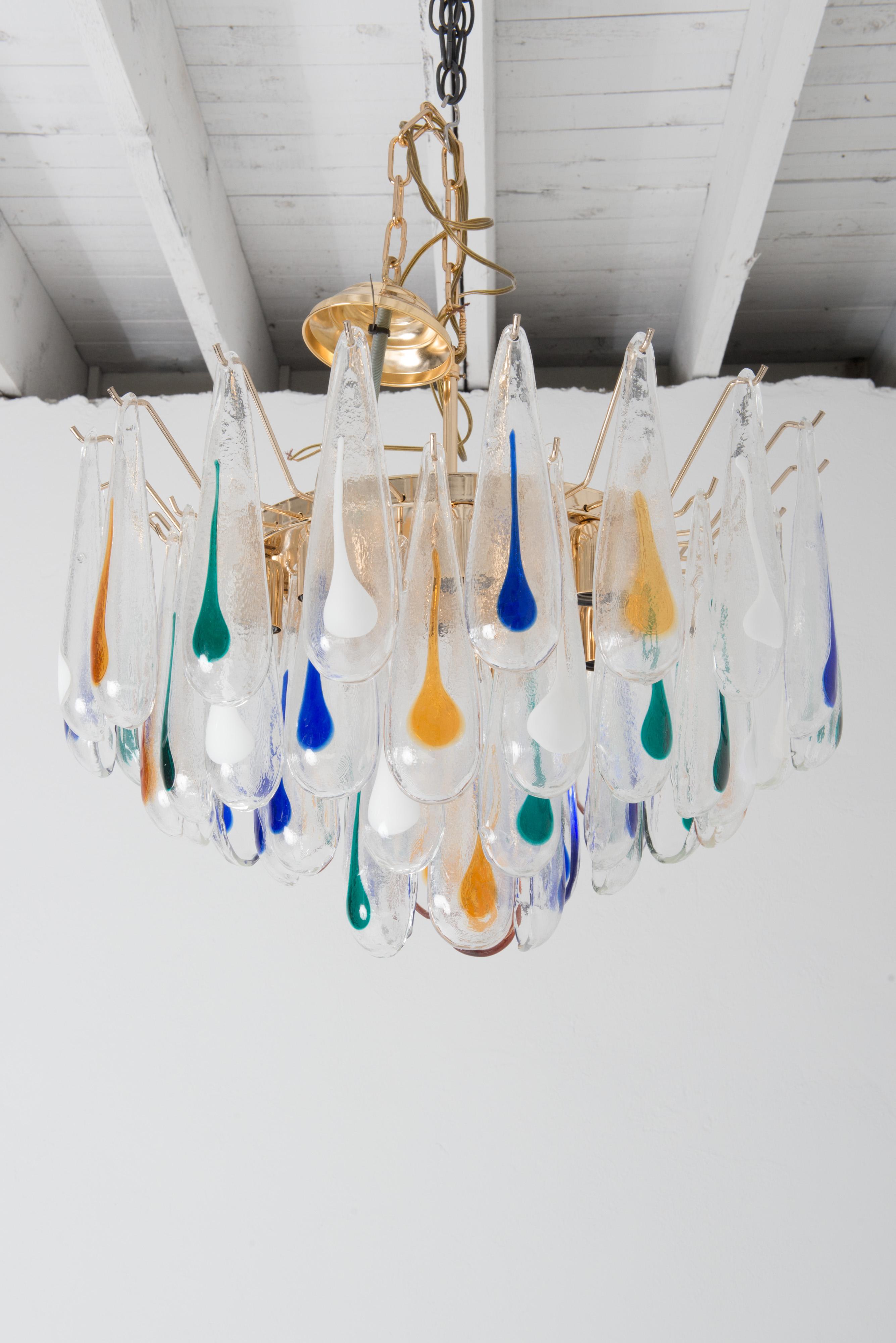 Lampadario di Murano in stile moderno degli anni '60, nuovo di zecca, con gocce di vetro da 9 pollici. Le gocce trasparenti sono infuse con grandi e drammatici colori blu, verde, giallo intenso e bianco.
gocciolamenti. Tutti sono appesi a un grande