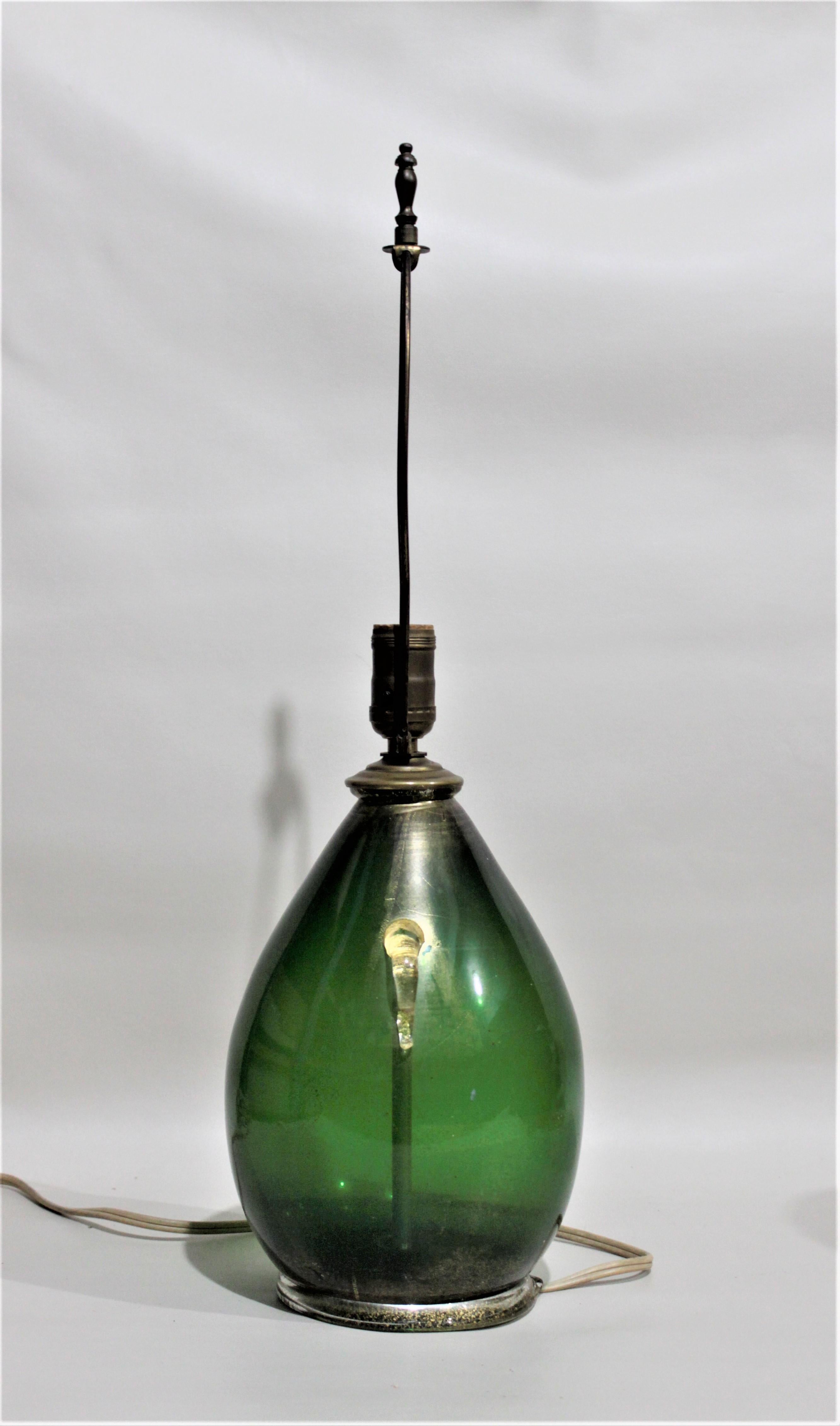 This Mid-Century Modern era Murano art glass table lamp is done in the style of Angelo Seguso and attributed to him as the maker. This table lamp features a deep dark green body with gold aventurine at the top and the bottom with applied clear art