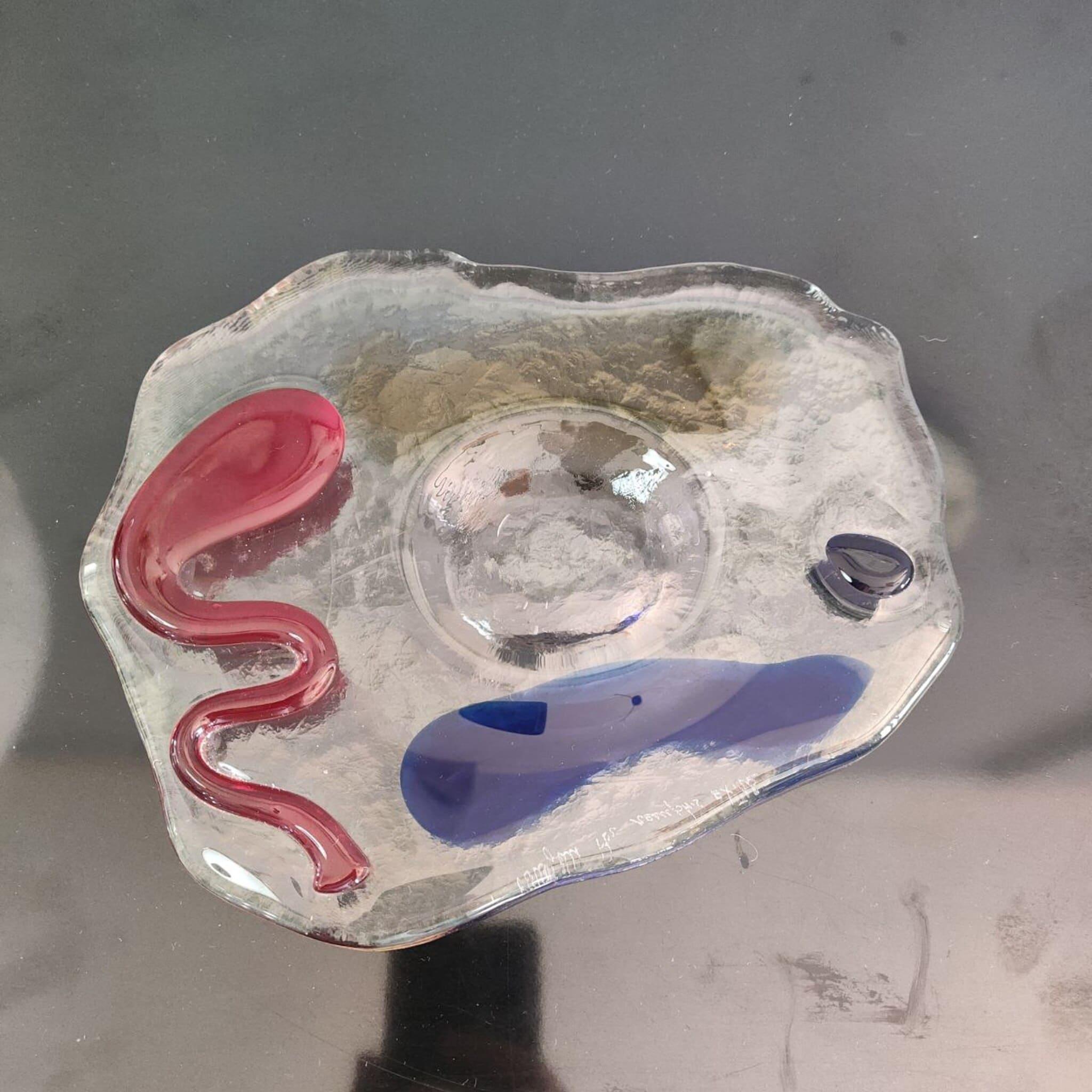 Icono del diseño italiano posmoderno, este cubilete/cenicero fue concebido en los años 80 por Luigi Serafini para la línea Memphis Extrà. Fabricado a mano en Murano, mide 25 × 20 × 2,5 cm y muestra la audaz paleta característica del movimiento: una