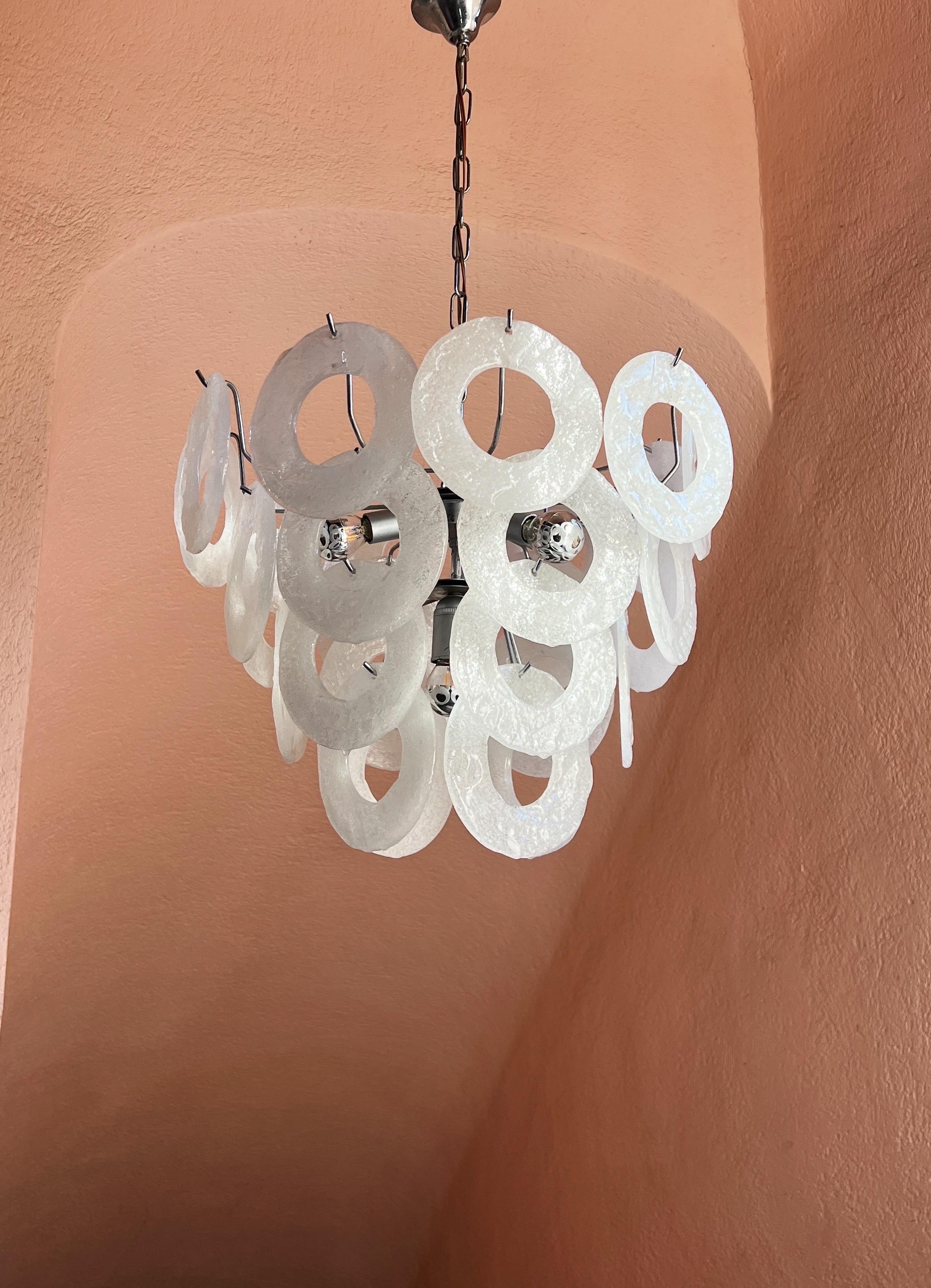 Esta elegante lámpara de cristal de Murano es un bello ejemplo de la artesanía italiana de la isla de Murano, famosa en todo el mundo por su tradición artesanal vidriera. La lámpara presenta múltiples discos de vidrio formados a mano en un blanco