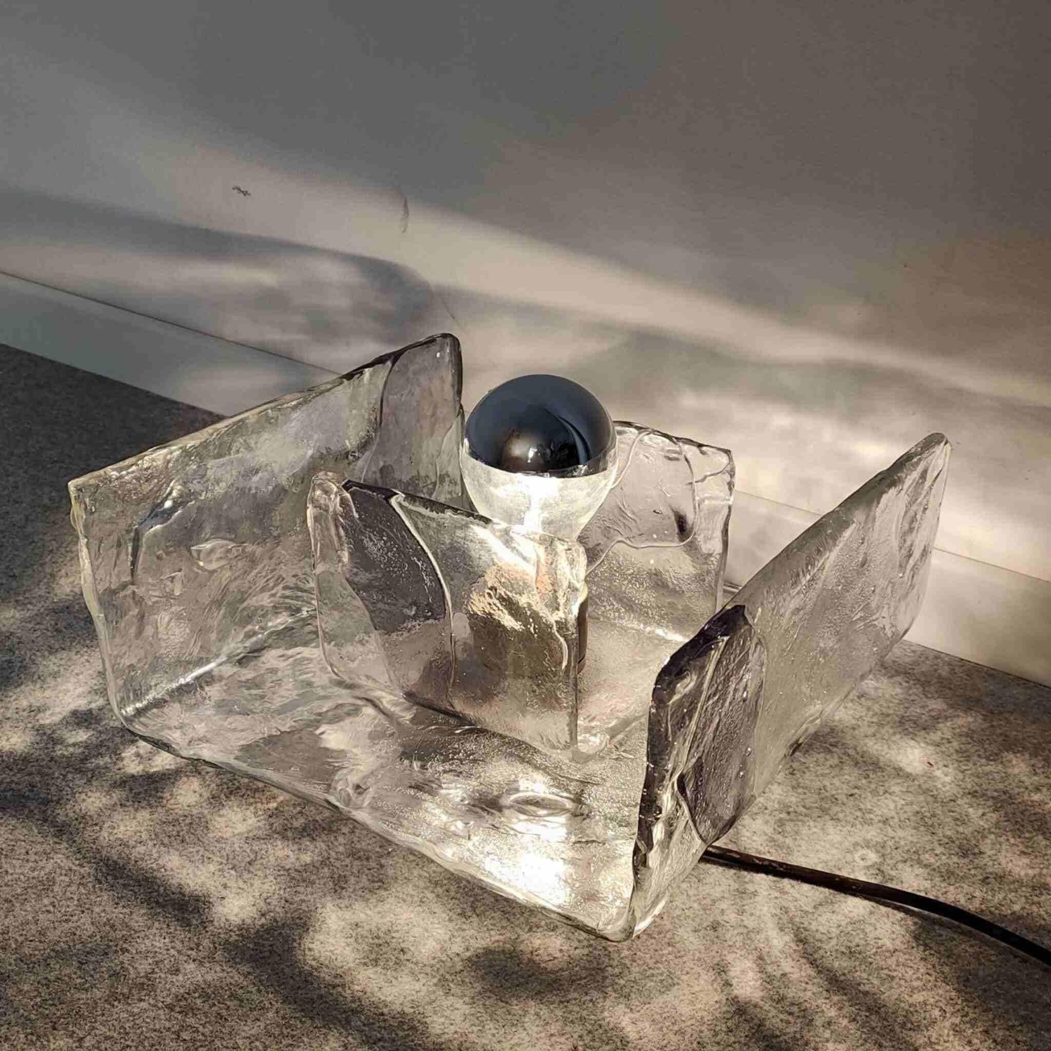 Lámpara de sobremesa de cristal de Murano de Mazzega, Italia, años 70. Diseño escultural con paneles de cristal texturizado formados a mano y portalámparas cromado.

Elegante lámpara de sobremesa de cristal de Murano, diseñada y fabricada por