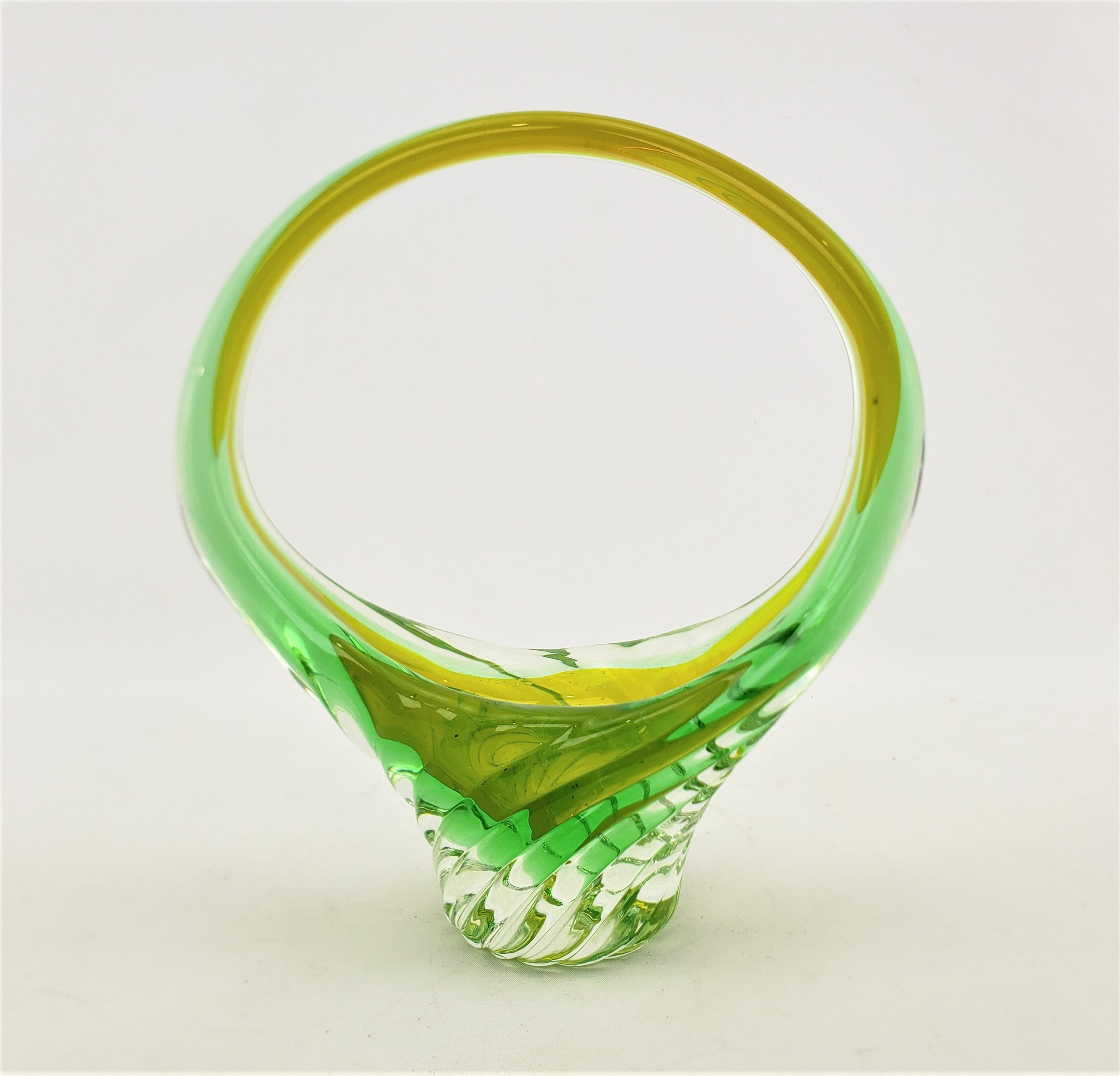 This art glass basket styled vase is unsigned, but presumed to have originated from Murano Italy and dating to approximately 1965 and done in the period Mid-Century Modern style. The vase is done with a thick clear glass with two submerged bands,