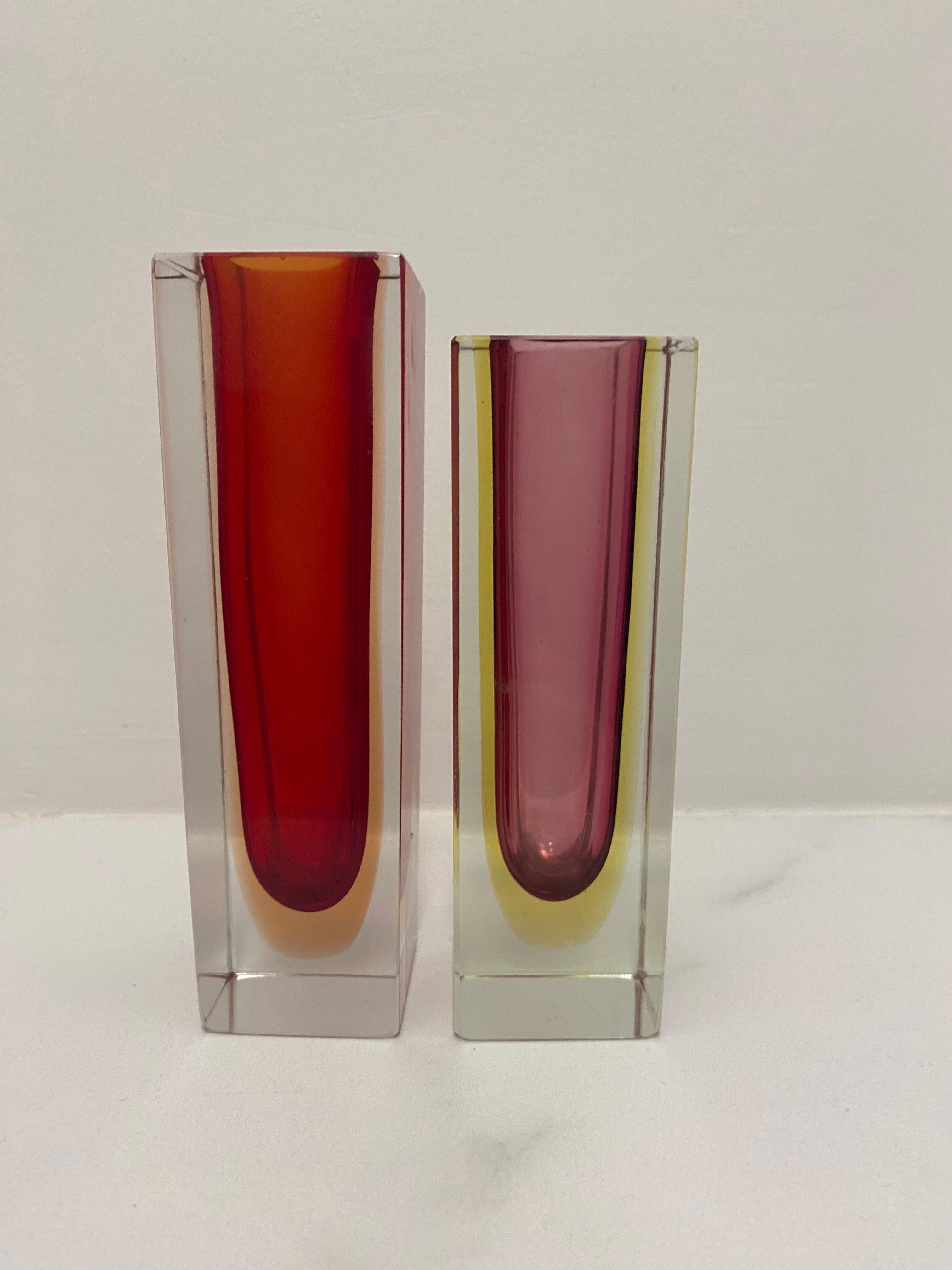 Bellissimo set di due vasi in vetro sfaccettato di Murano della metà del secolo scorso. Realizzato con la tecnica del vetro Sommerso.

Uno è rosso e arancione
Il più piccolo è di colore viola e giallo e ha un'altezza di 12 cm.