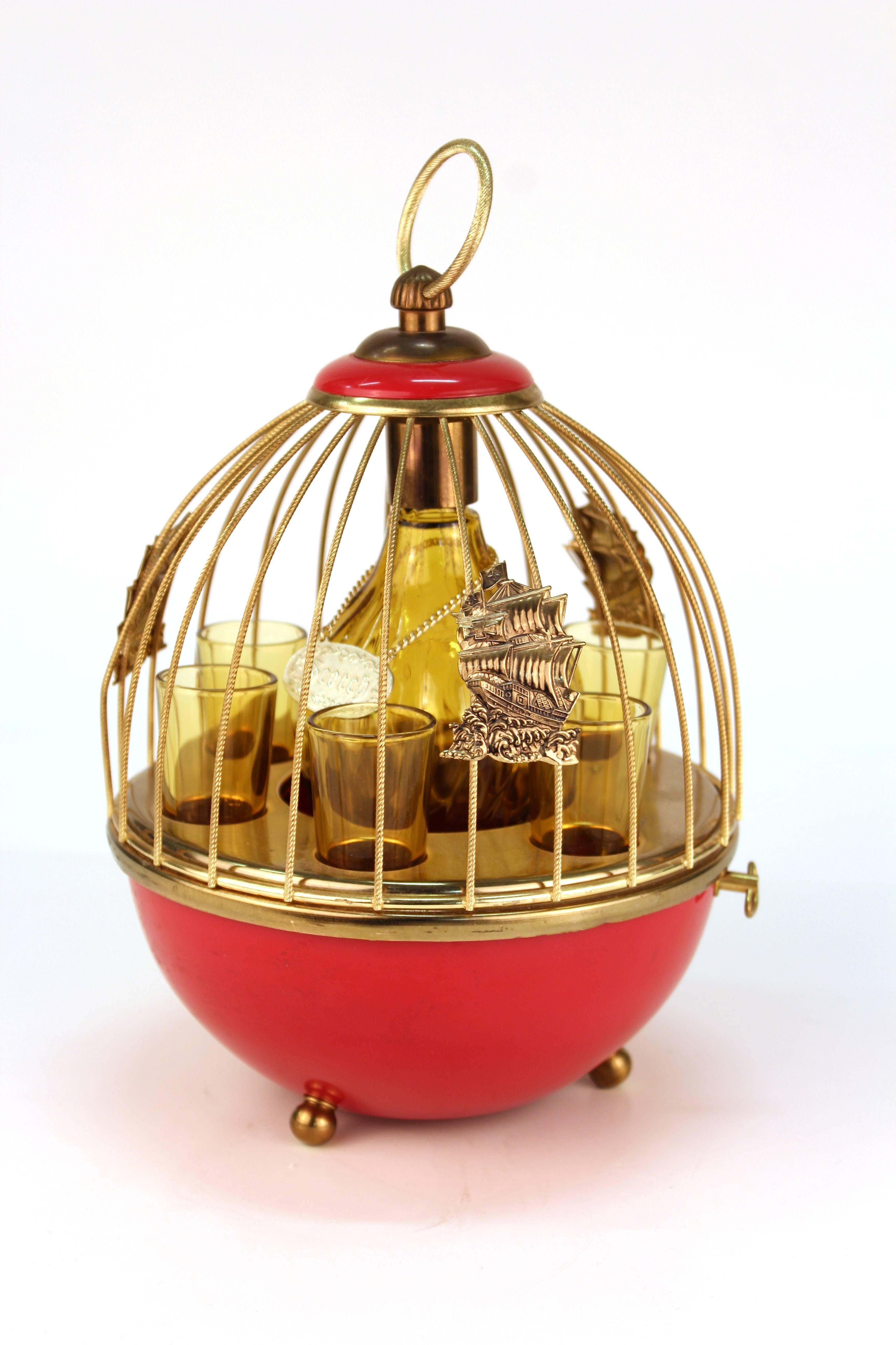 A Mid-Century Modern decanter set within a bird cage setting, consisting of a decanter and six glasses. The decanter has a 'scotch' tag. The bird cage has decorative galleon ornaments. The piece plays 'The Days of Wine and Roses'. In good vintage