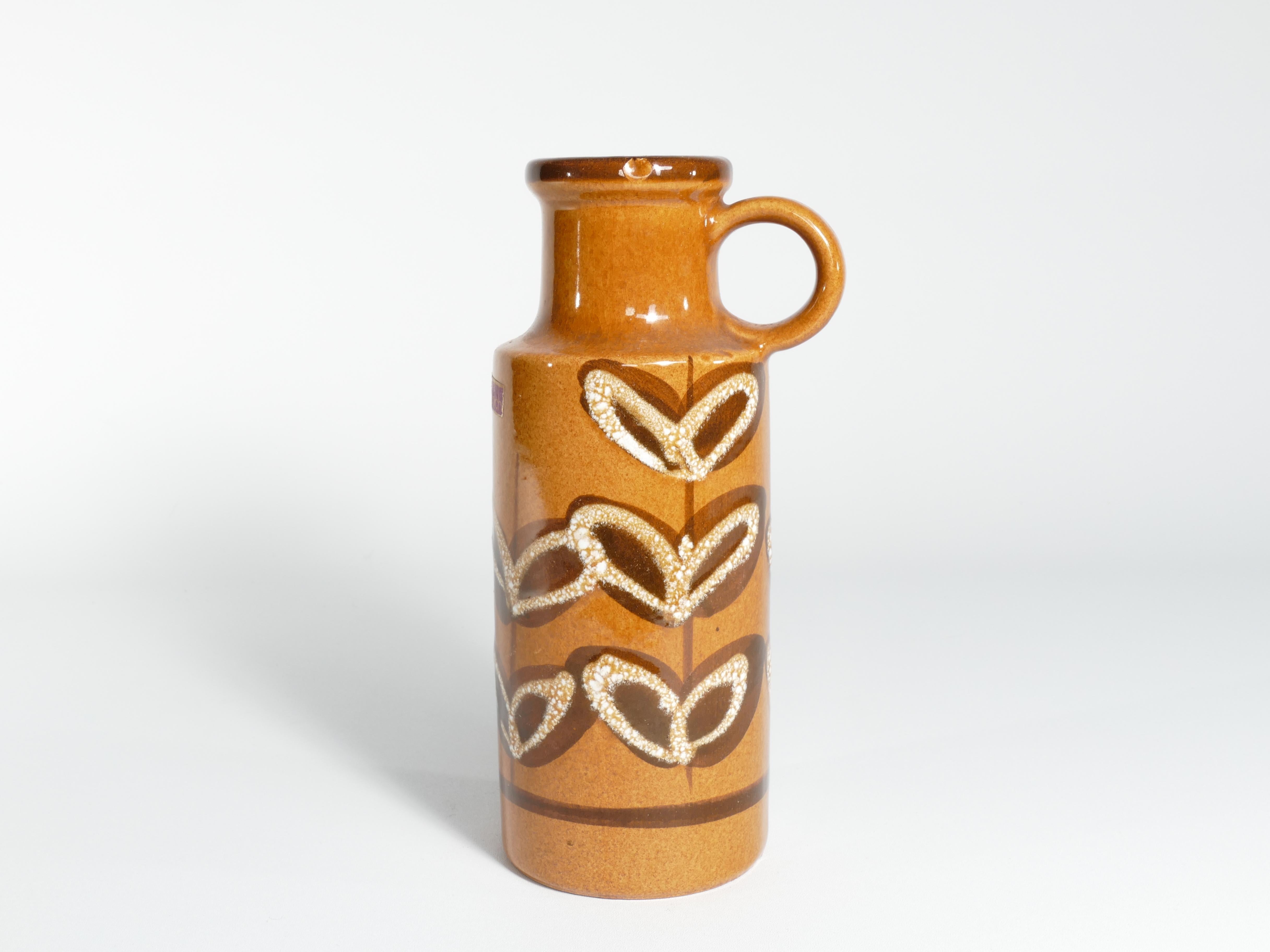 Senfgelbe Vase mit schönen braunen und weißen Blattdetails.
Dies ist ein schönes Beispiel für ein Sammlerstück westdeutscher Kunstkeramik von Scheurich Keramik.

Der Sockel ist mit der Aufschrift 