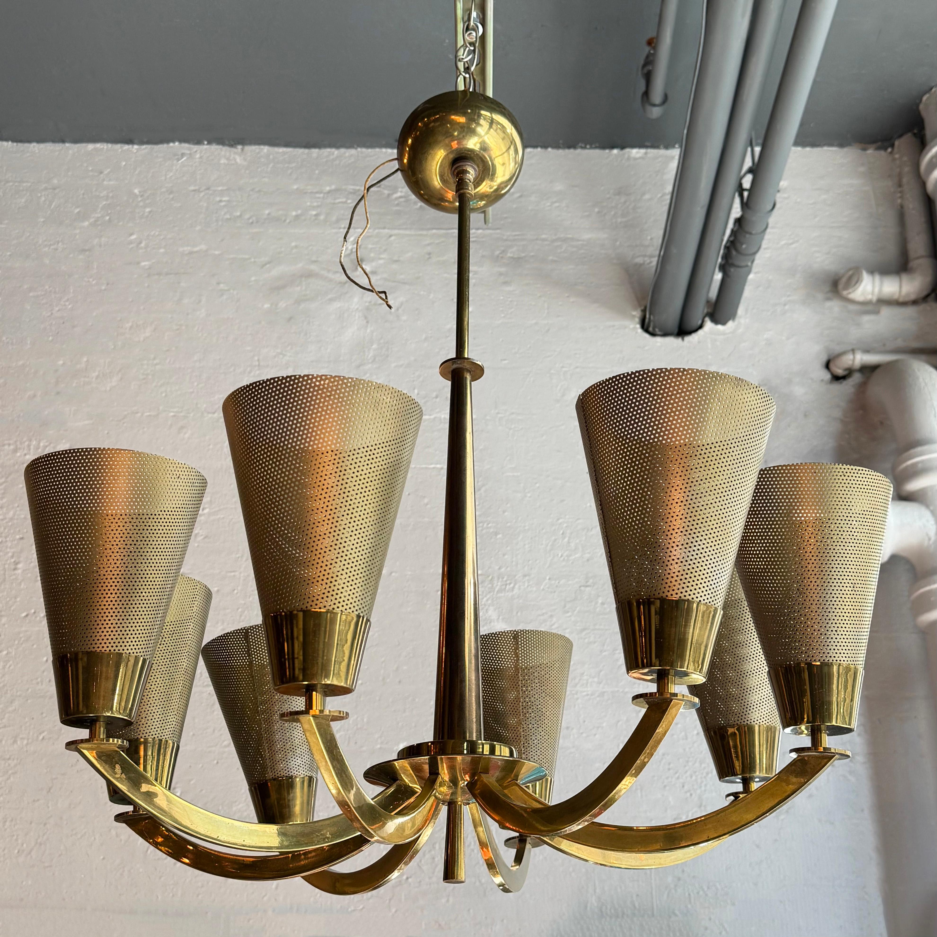 This wonderful mid-century modern chandelier features eight upward curled faceted brass arms eminating from a tall tapered polished brass center stem with brass saucer, cylinder finial and matching canopy. The shades for each arm are perforated