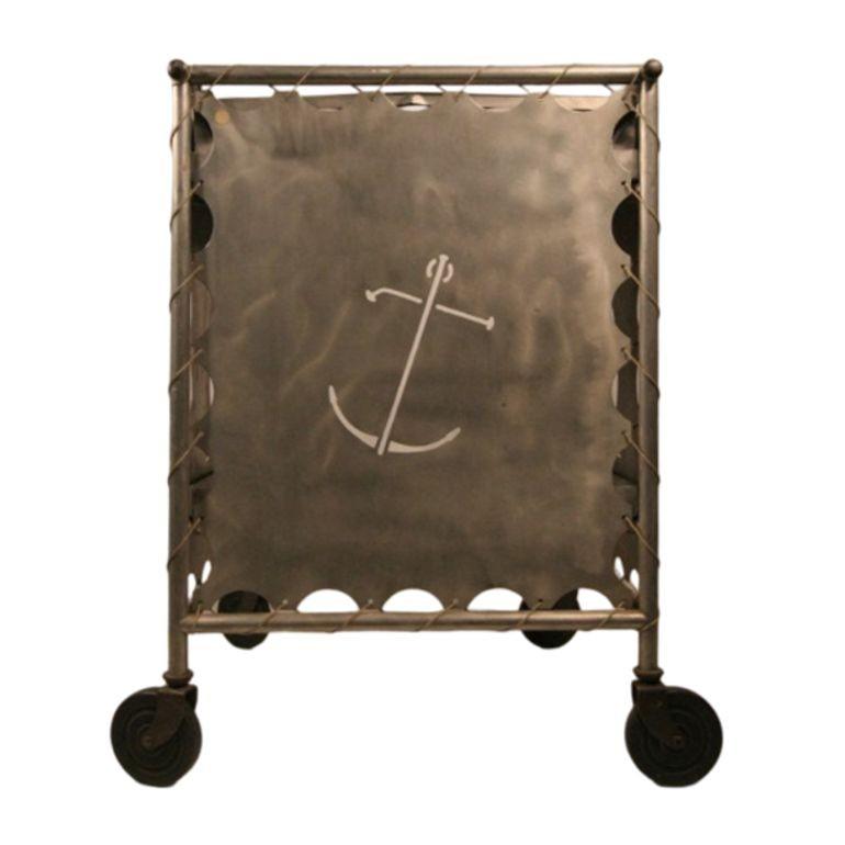 This Post-War, Mid-Century Modern nautically themed bar cart is rendered in aluminum. The cart features plenty of storage with a built-in bottle holder and two-tier shelving. Nautical cut-outs of sailboats and anchors appear on the side panels. The