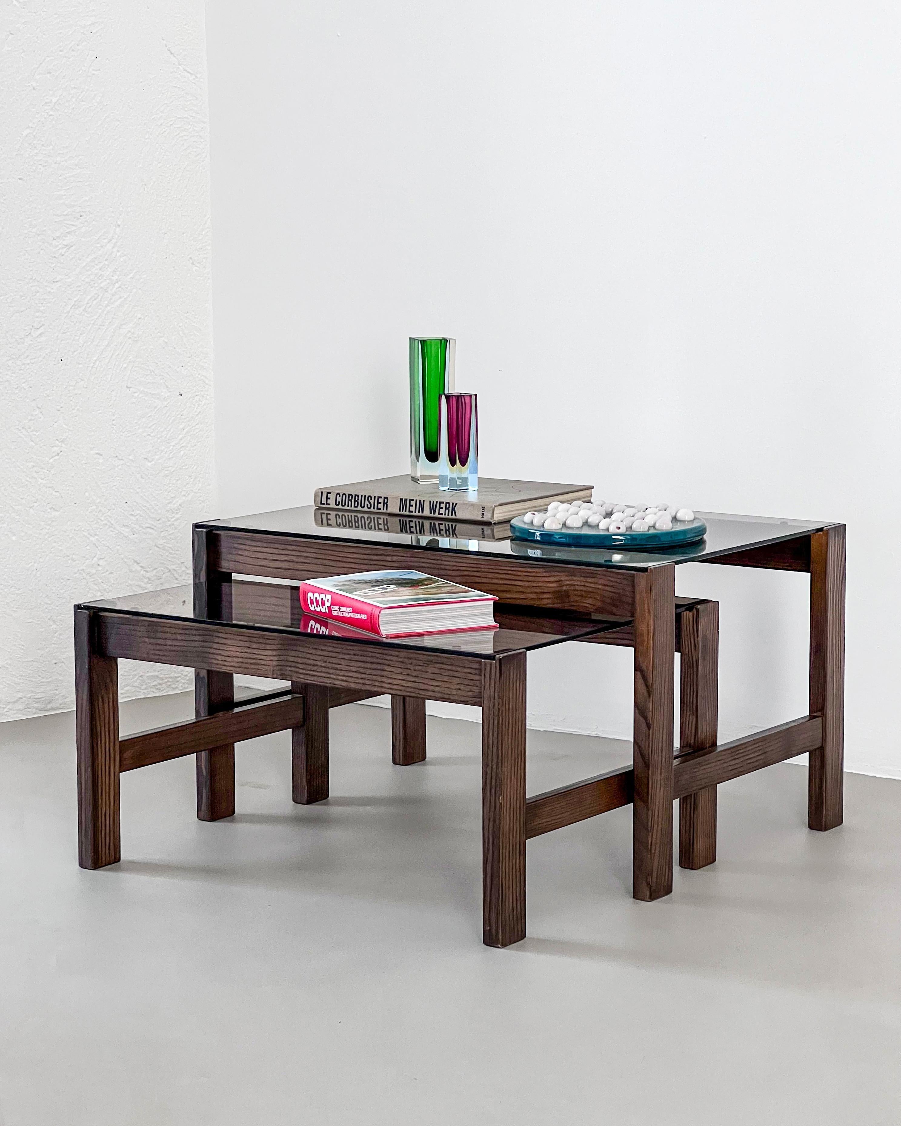 Offered for sale is a beautiful set of two nesting coffee tables, crafted from solid wood (most likely walnut) with lightly smoked glass tops. The design, essential yet refined, reminds pieces created during the sixties by Gianfranco Frattini and
