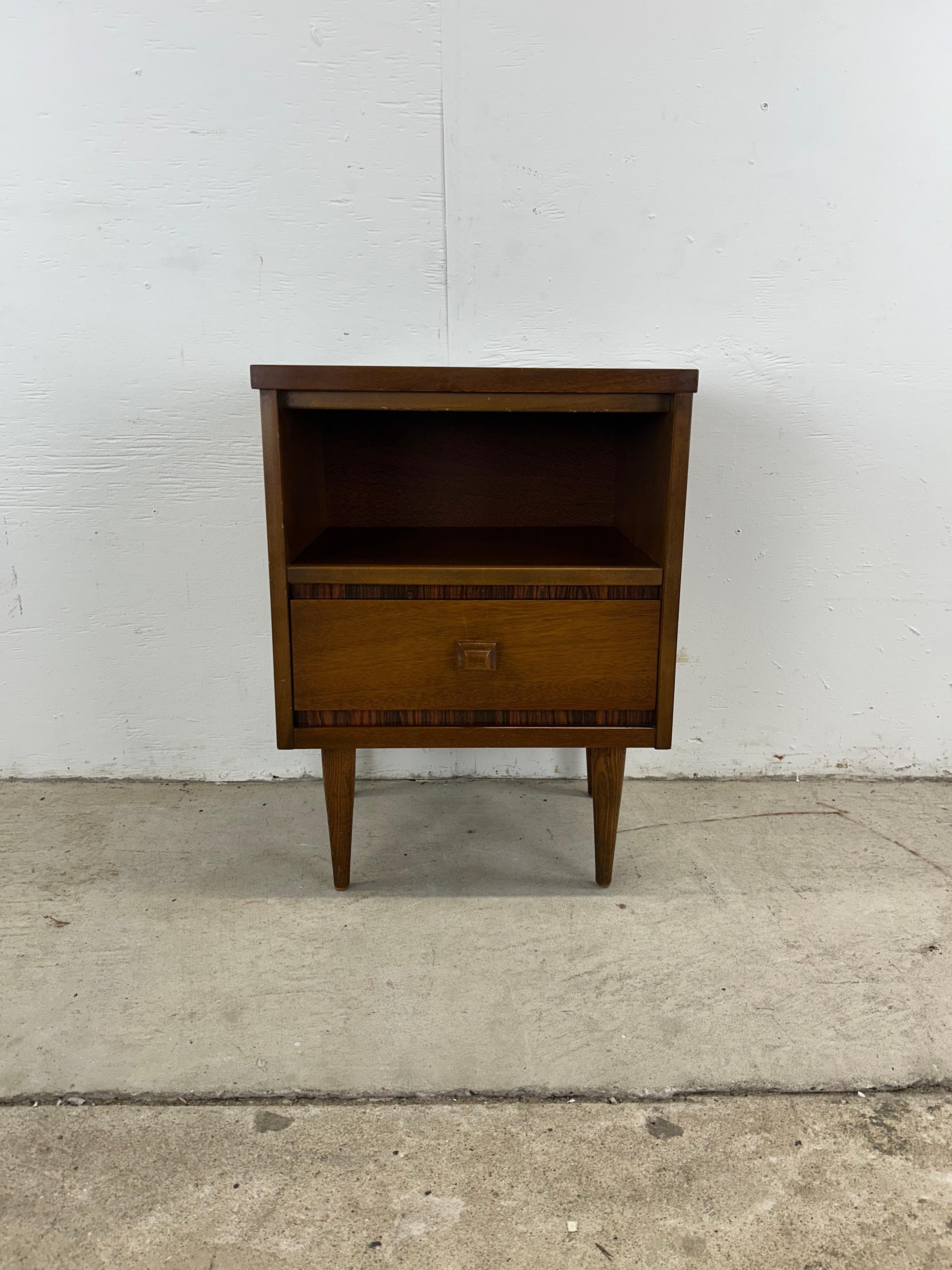 This mid century modern nightstand by Bassett Furniture features hardwood construction, walnut veneer with original finish, unique rosewood trim around the edges, single dovetailed drawer with sculpted wood pull, durable Formica top, and tall