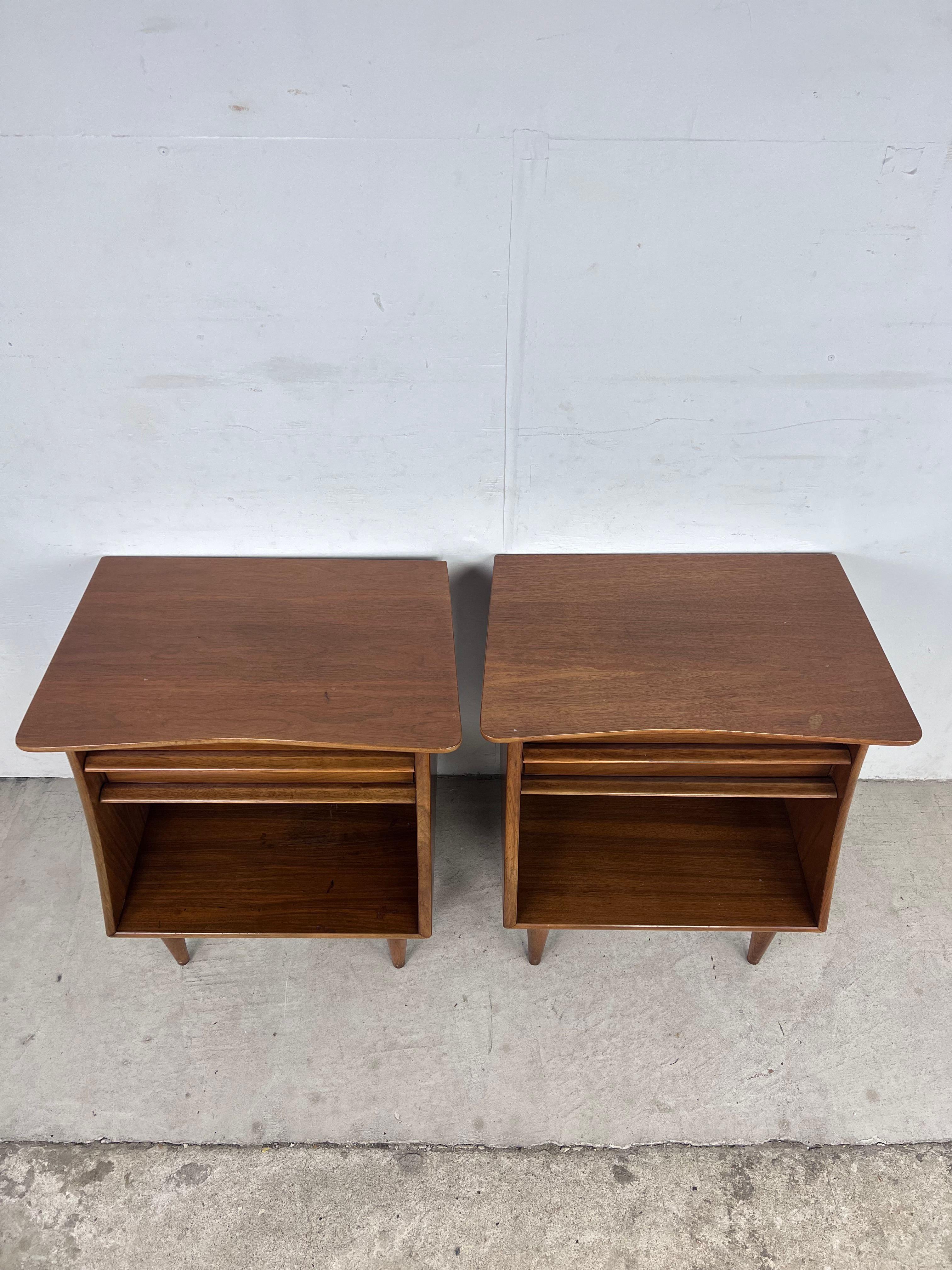 This pair of mid century modern nightstands from the Foreteller line by Kent Coffey feature hardwood construction, original walnut finish, single dovetailed drawer with unique carved pull, opened storage shelf, and tall tapered legs.

Matching
