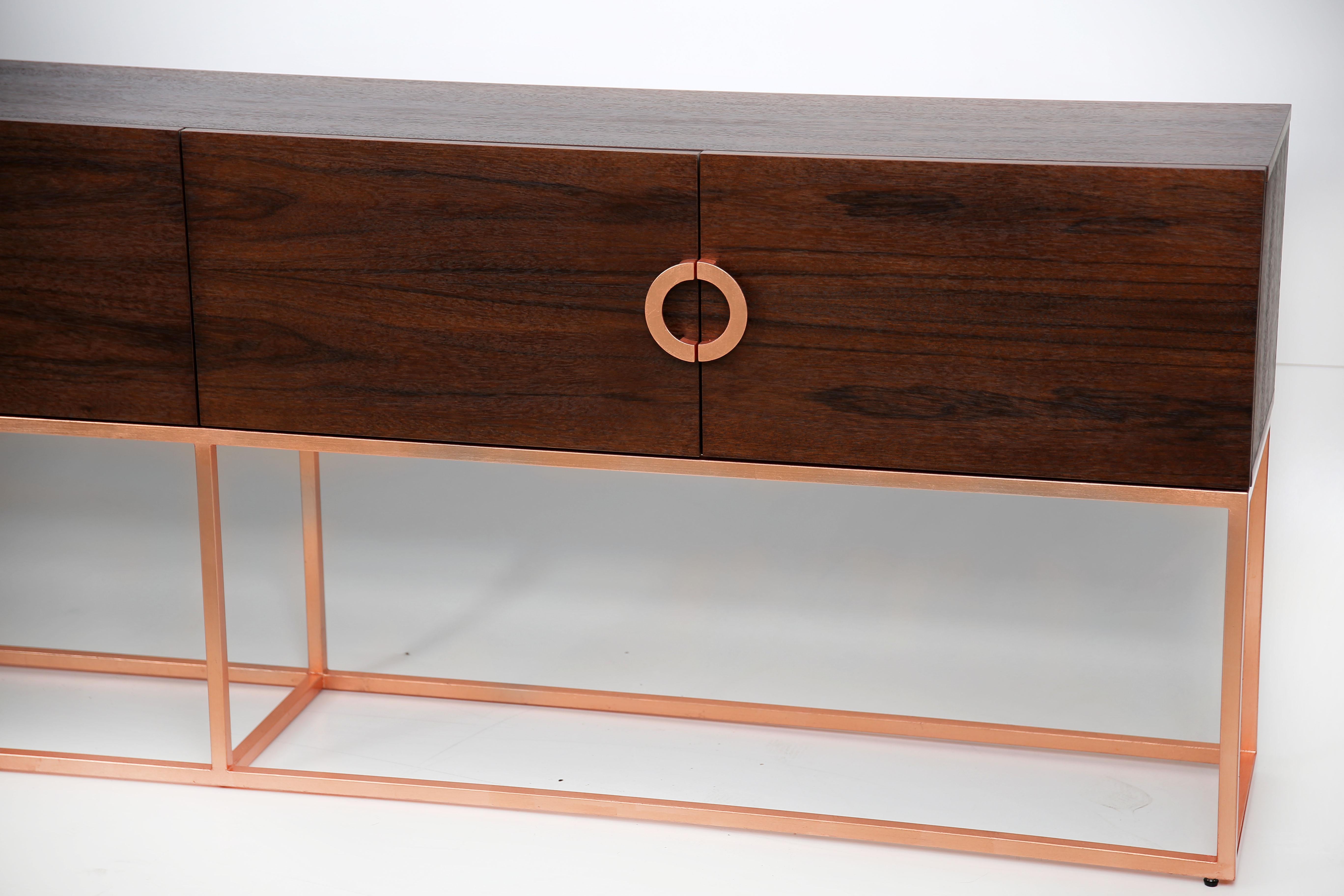 Norse TV stand presents your everyday space with ample storage. Constructed of engineered wood and finest American walnut veneers. The TV stand features four doors for your gaming consoles, video players and DVD collections. Copper leaf handles