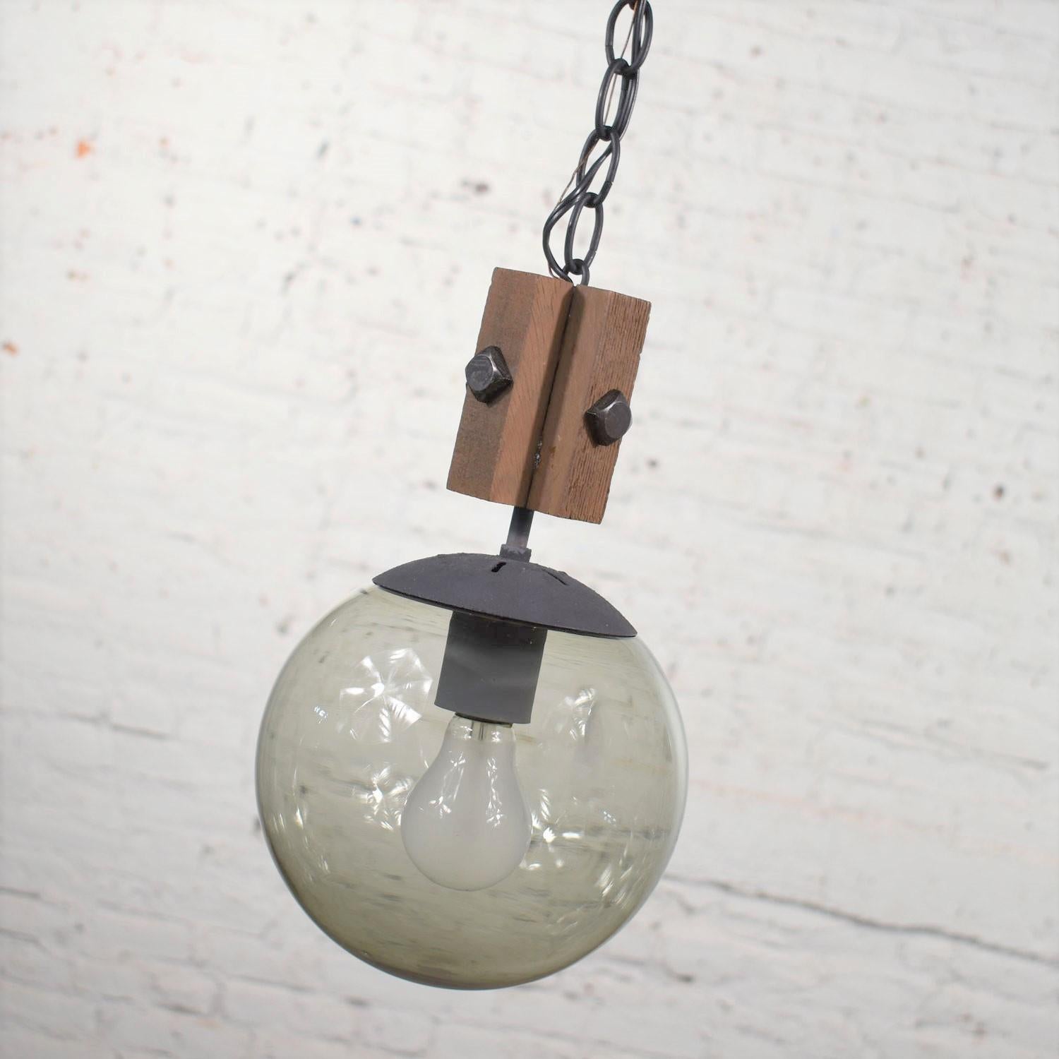 Handsome Mid-Century Modern NOS (new old stock) slightly Brutalist or rustic black, wood, and smoked glass globe pendant light with black chain and canopy. It is made by Lighting-Accessories, Inc. a Hamilton Cosco company. It is in wonderful vintage
