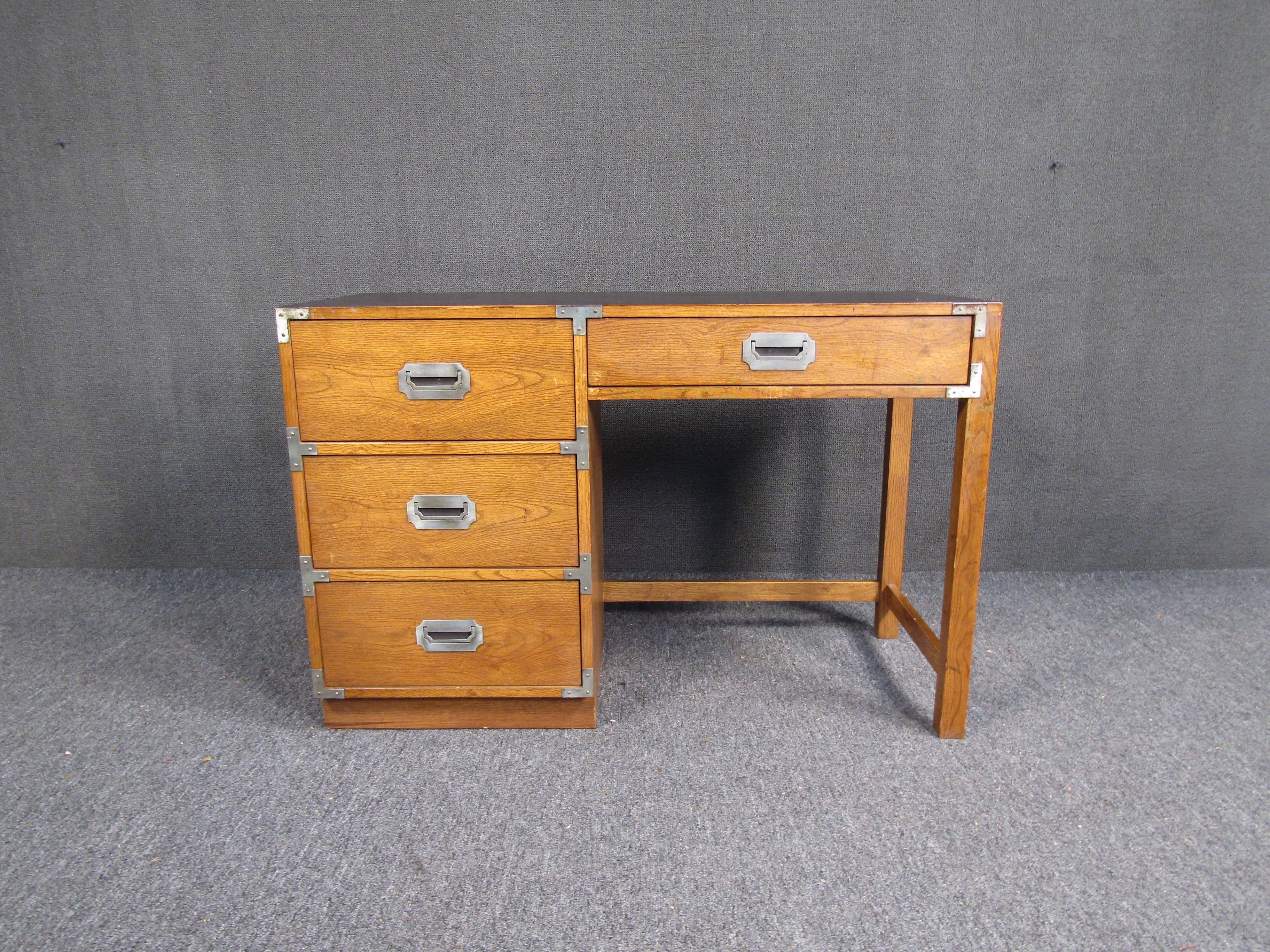 With four large drawers, sculpted legs, and a black-stained writing surface, this vintage campaign desk is perfect for any home office or study. Beautifully finished oak woodgrain complements Mid-Century design to make this piece stand out anywhere.