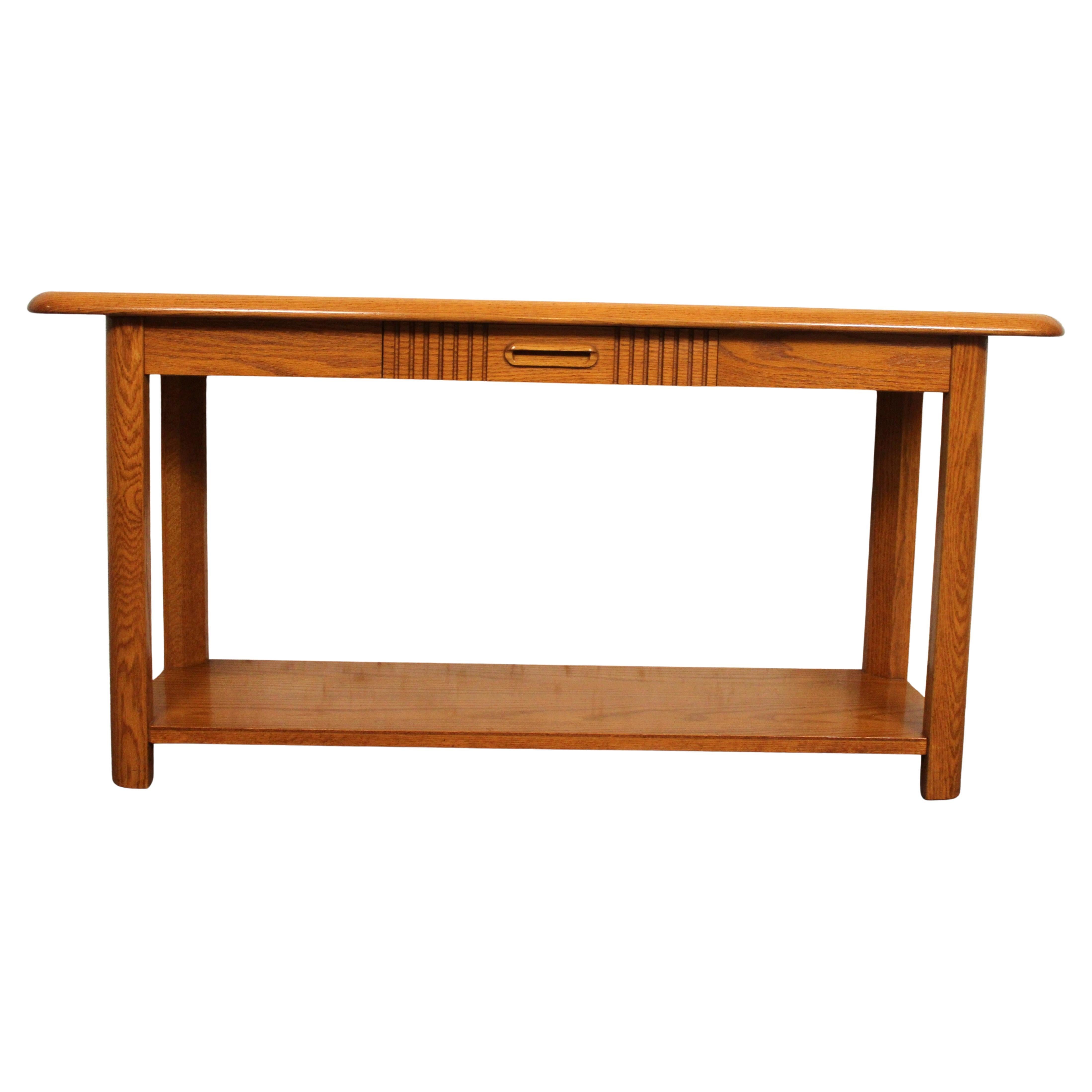 Consola de roble moderna de mediados de siglo, de Mersman, con un único cajón central con tirador esculpido y detalle en forma de lengüeta. Apoyada en patas redondeadas con un estante inferior, esta pieza combina funcionalidad con un estilo