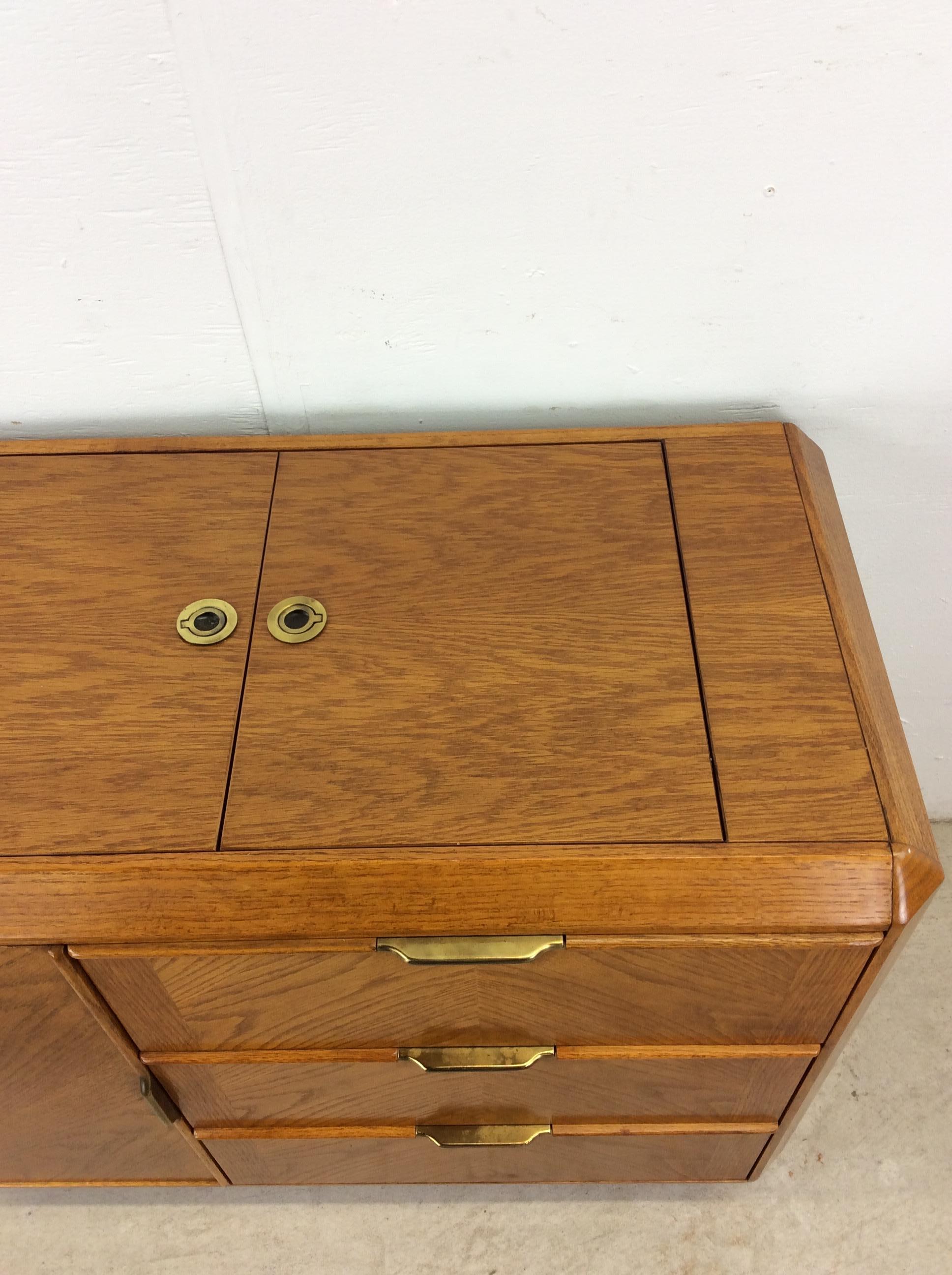 Questo bar moderno di metà secolo di Stanley Furniture presenta una struttura in legno massiccio, impiallacciatura in Oak con finitura originale, tre cassetti a coda di rondine e un'anta con ferramenta in ottone, piano in espansione in due pezzi con