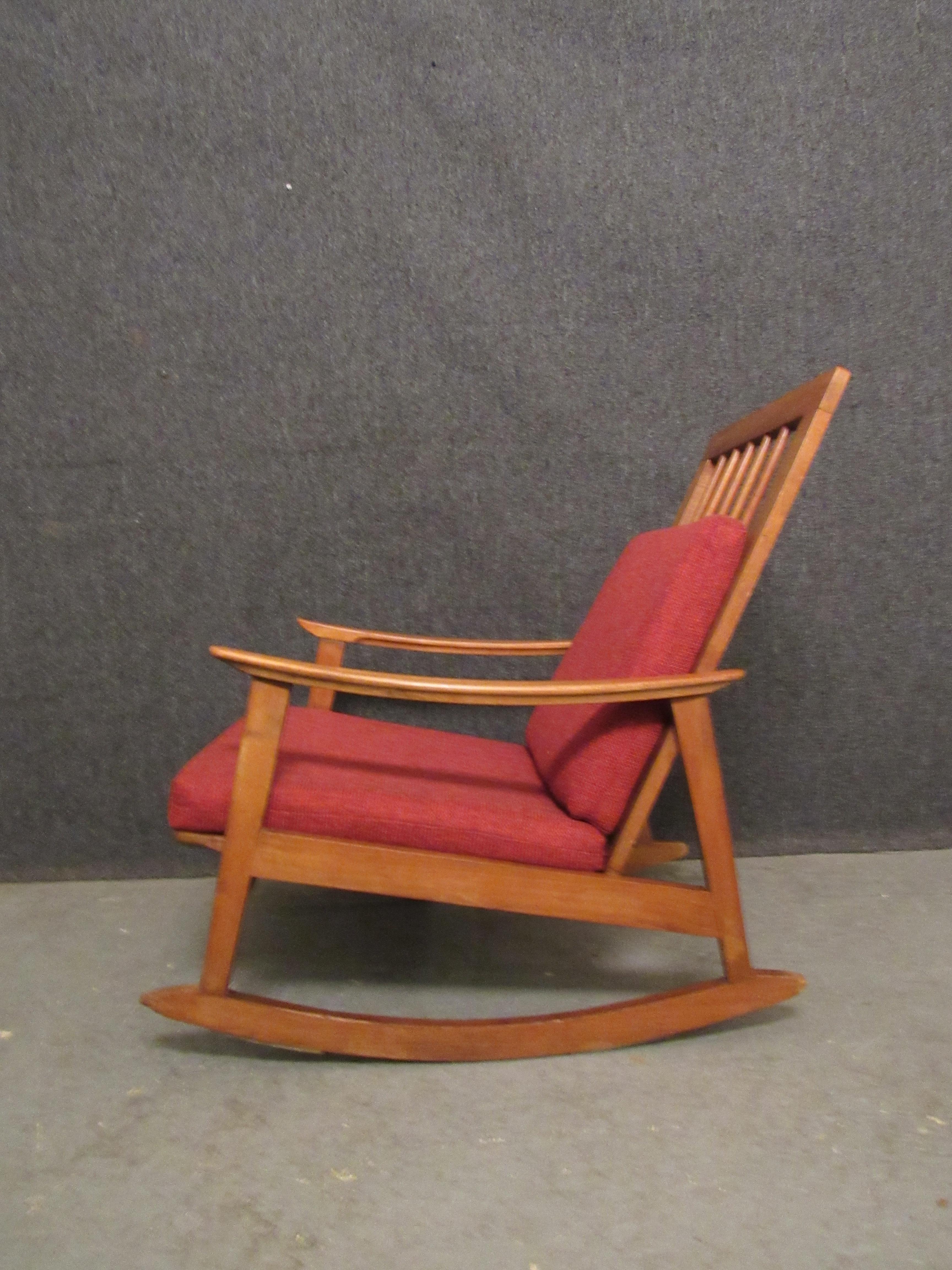 Kick back and relax with the vintage comfort of this mid-century modern oak rocker. The sloping arms and feet gives classic Scandinavian flare into any space. A tall spindle back peaks out from behind the pair of wooly red cushions, creating a