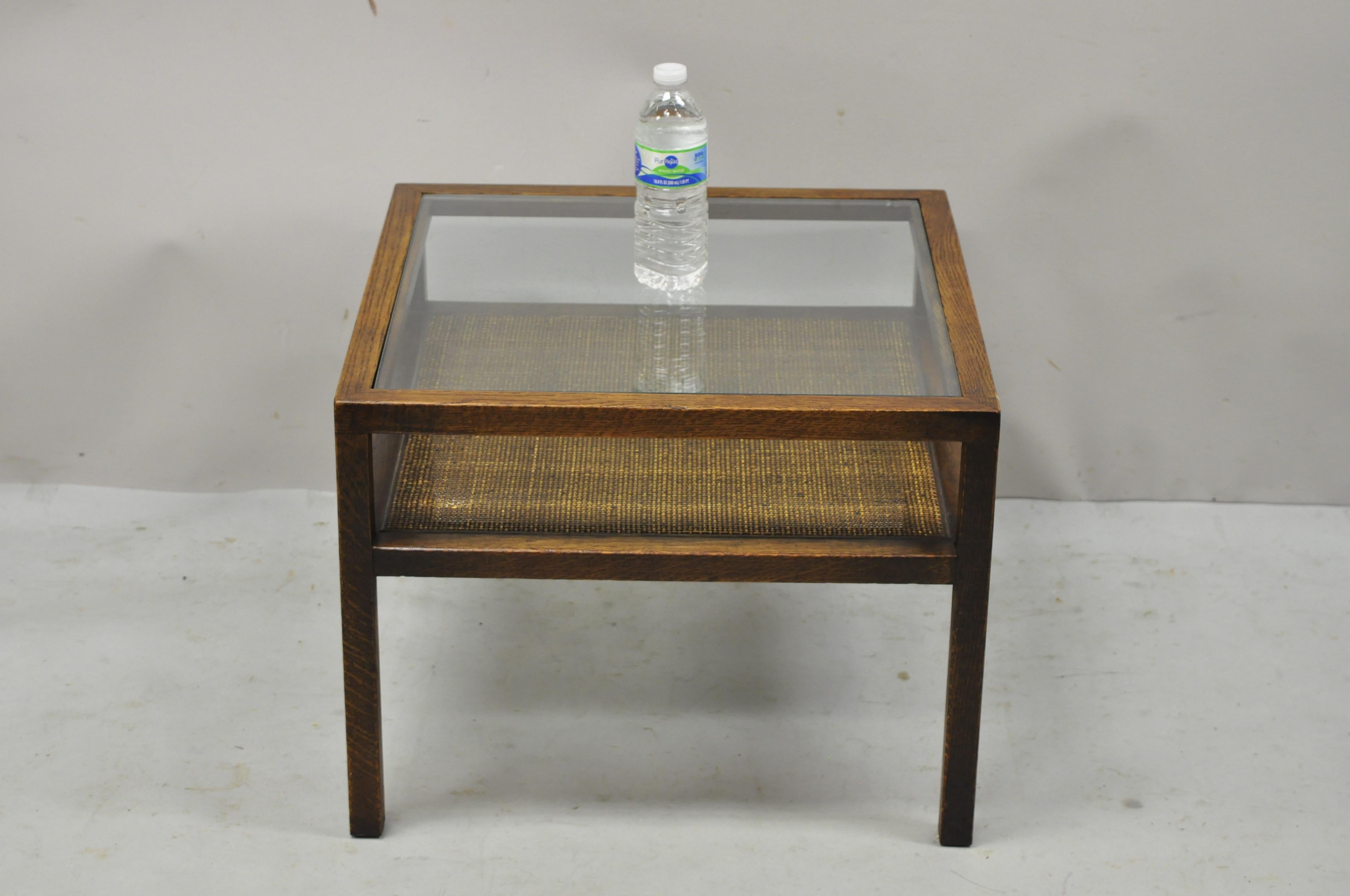 Mid-Century Modern oak wood and cane 2 tier glass top small square side table in the Dunbar style. Item features inset glass top, cane lower shelf, solid wood frame, beautiful wood grain, clean modernist lines. Circa mid 20th century. Measurements: