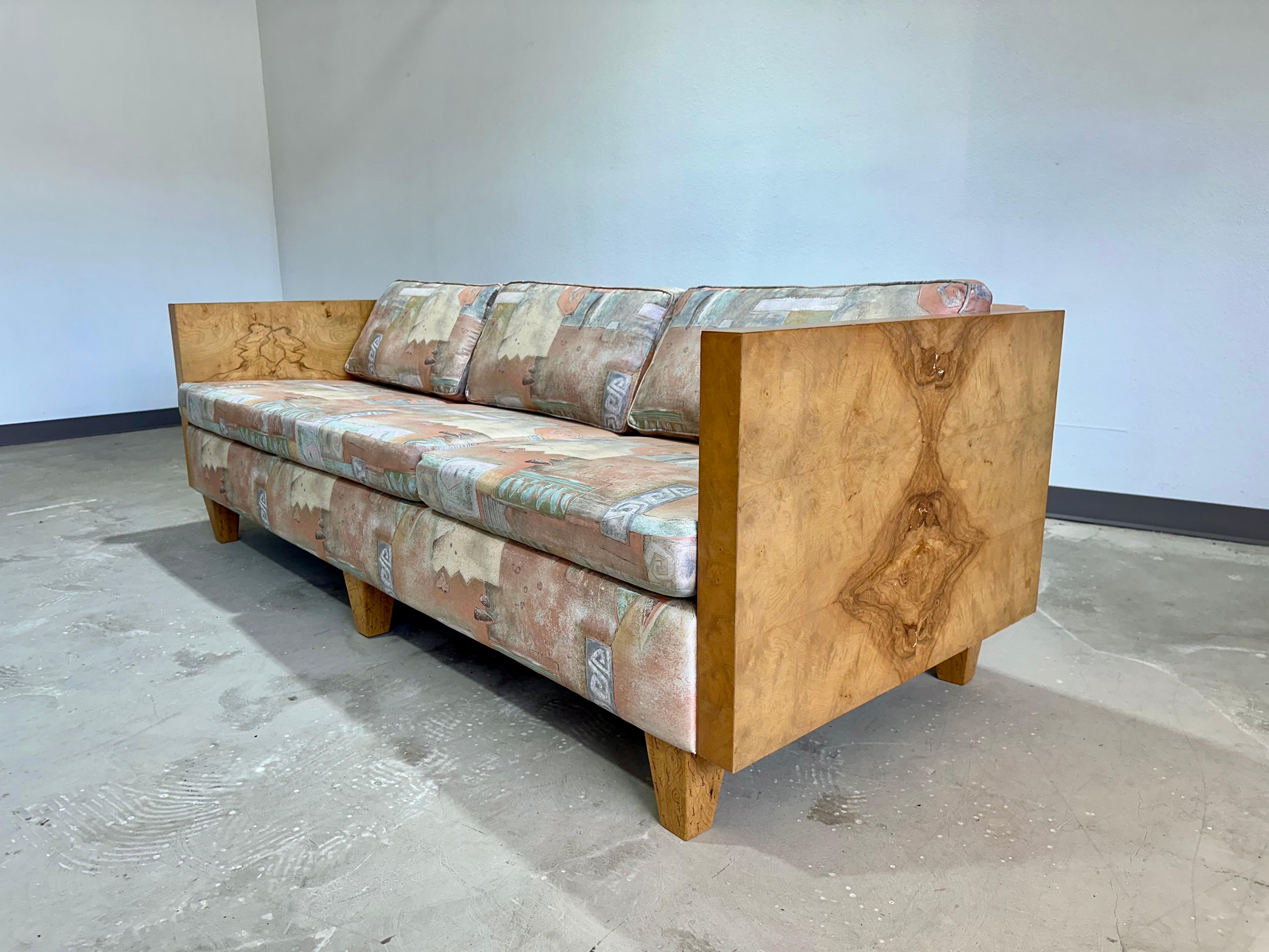 Mid Century Modern Milo Baughman Style Olive Burl Wood Cased Sofa. Impressive grain patterns on both sides, professionally reupholstered in the early 1990’s in pastel abstract print fabric. Original tags are no longer present. Two matching loveseats