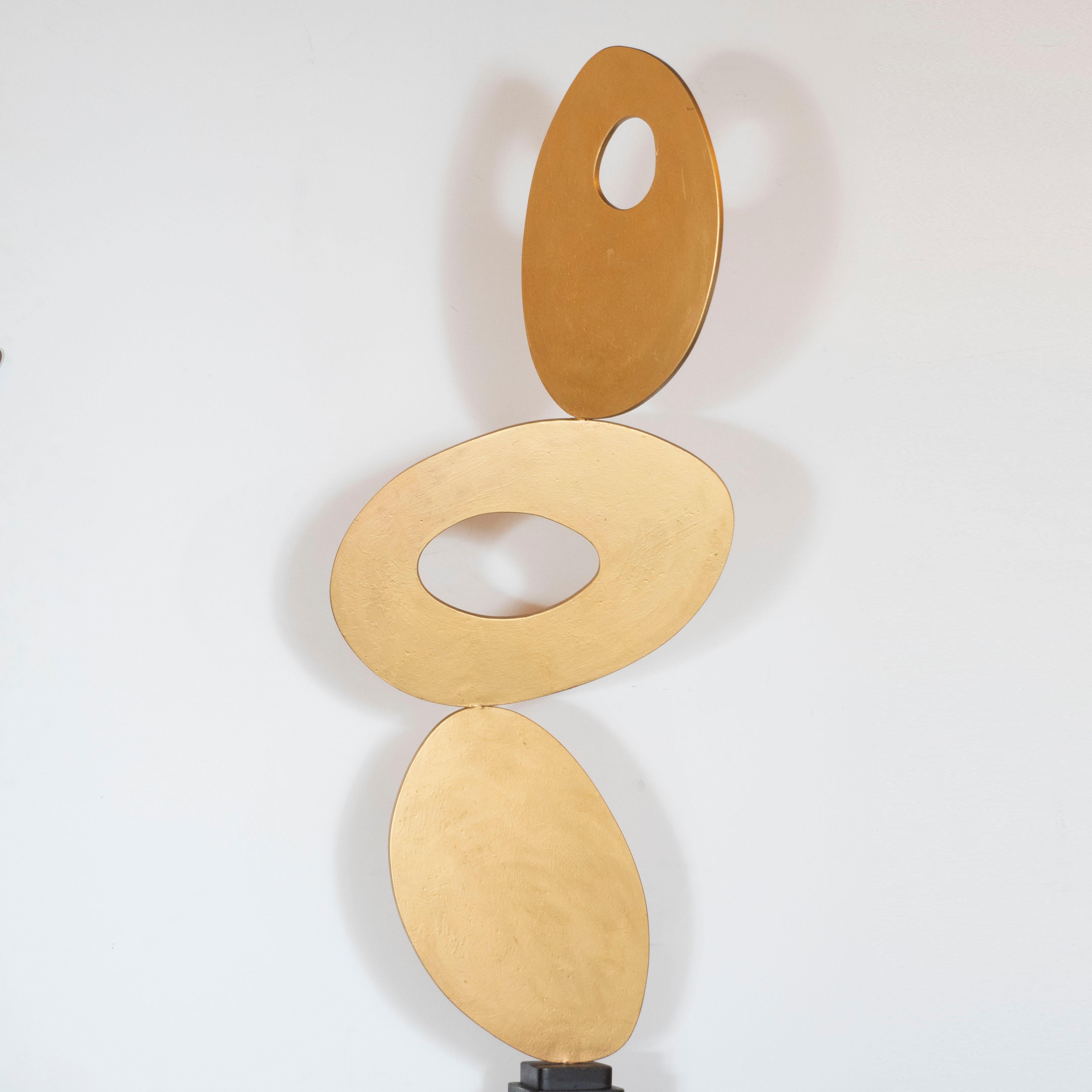 This stunning and dynamic Mid-Century Modern sculpture was realized by the esteemed New York artist, Harold Sklar (1930-2003), circa 1970. It features three stacked gilded steel ovoid forms- the top two of which have oval cutouts in the center-