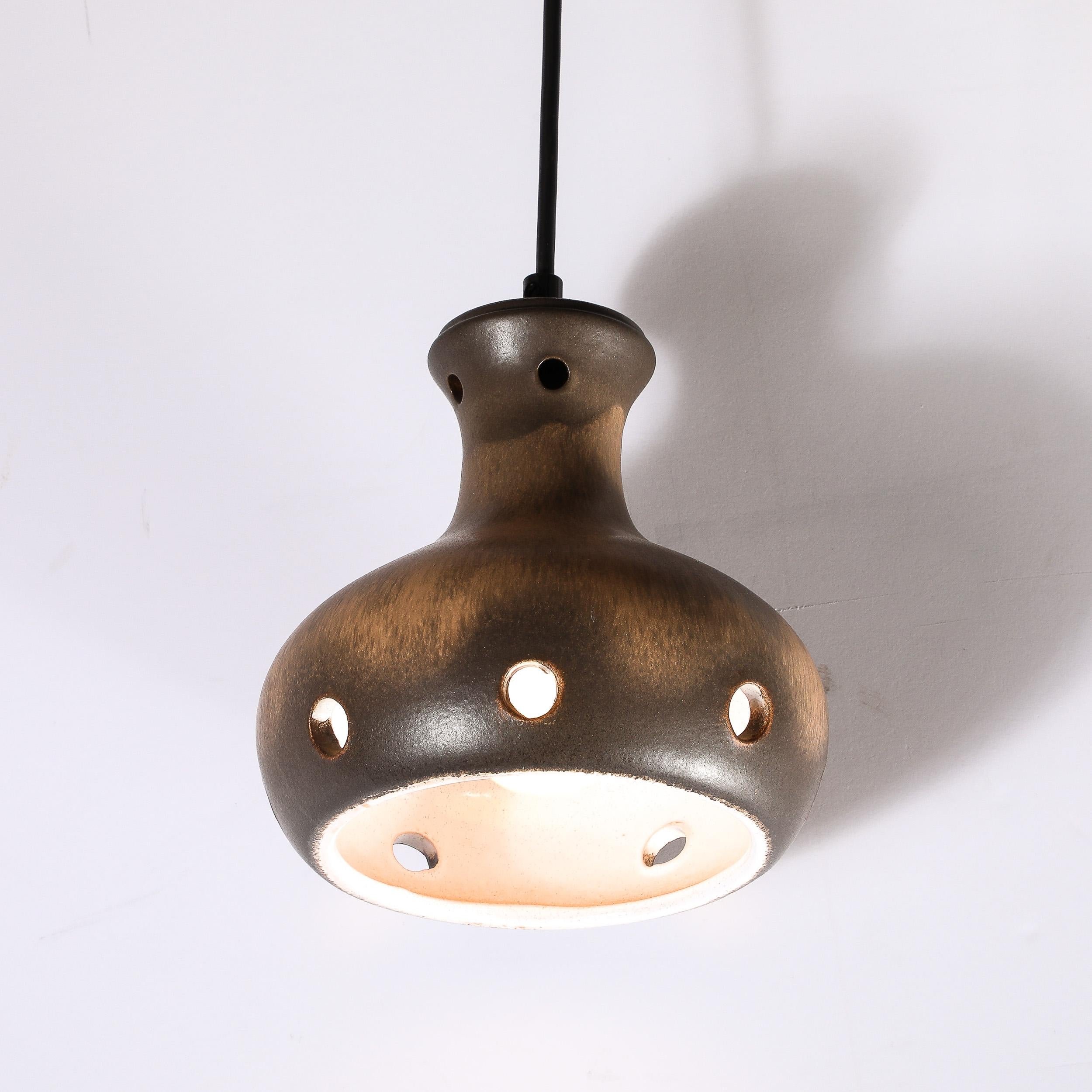 This pendant was handcrafted in ceramic and glazed, in Sweden , circa 1960. It offers a billowing form with seven circular perforations at its base, and four at its top, as well as variegated ochre tones with inflections of ivory throughout. The