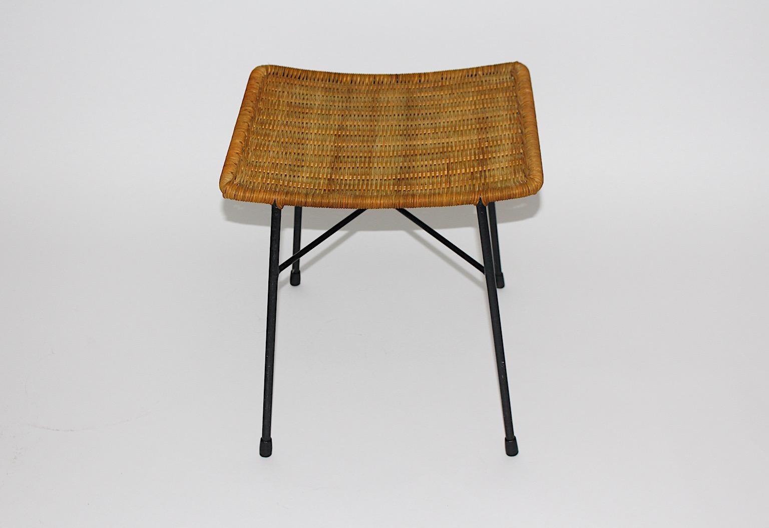 Mid Century Modern vintage organic stool or ottoman or footstool from rattan and black lacquered metal frame 1950s Austria.
While the slightly curved seat shows wonderful organic rattan network, the black lacquered metal frame features a crossed