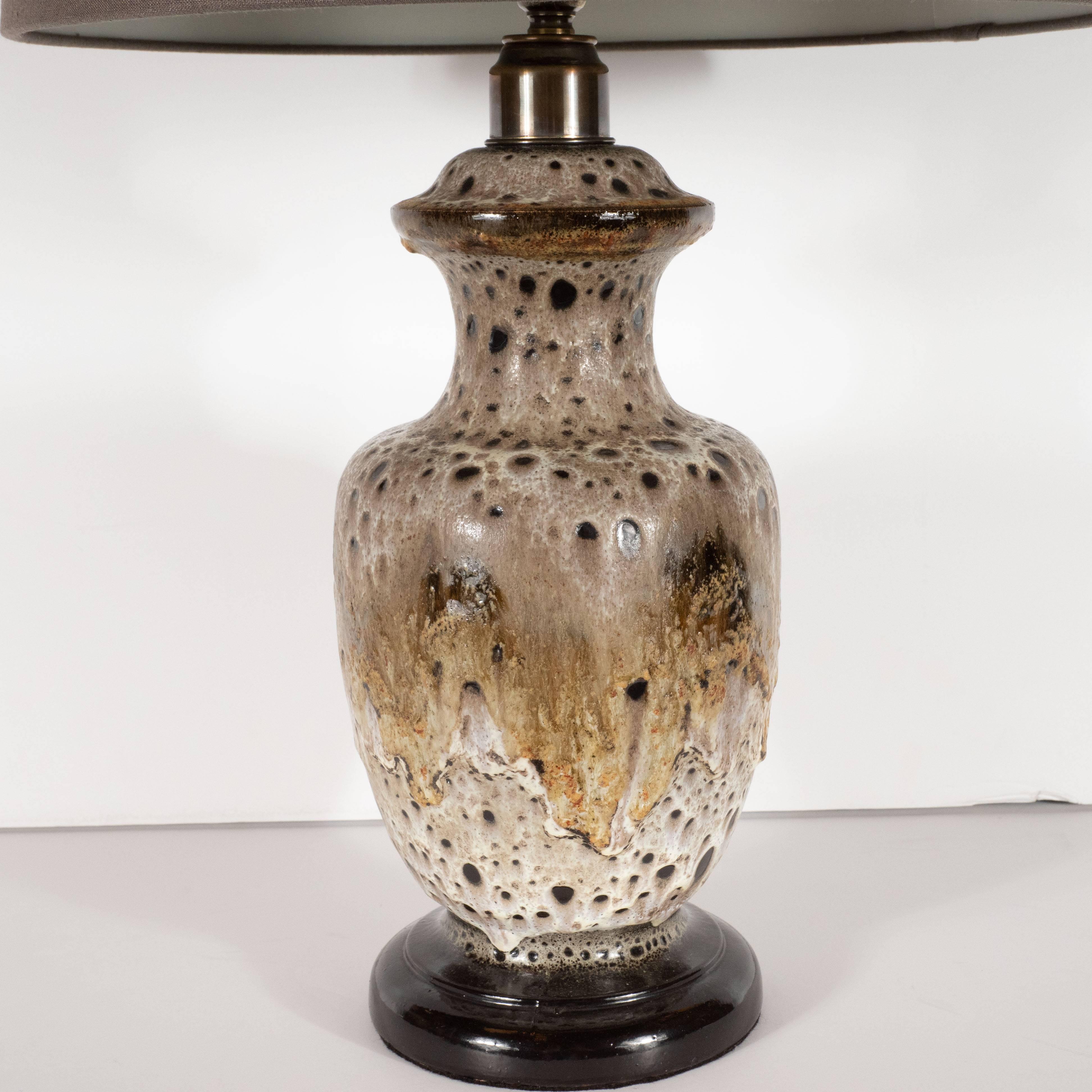This striking ceramic table lamp was handcrafted and glazed in Germany, circa 1950. It offers an urn form body with a raised circular detail circumscribing the top of the neck. The beveled and stepped base of the piece is finished in a rich burnt
