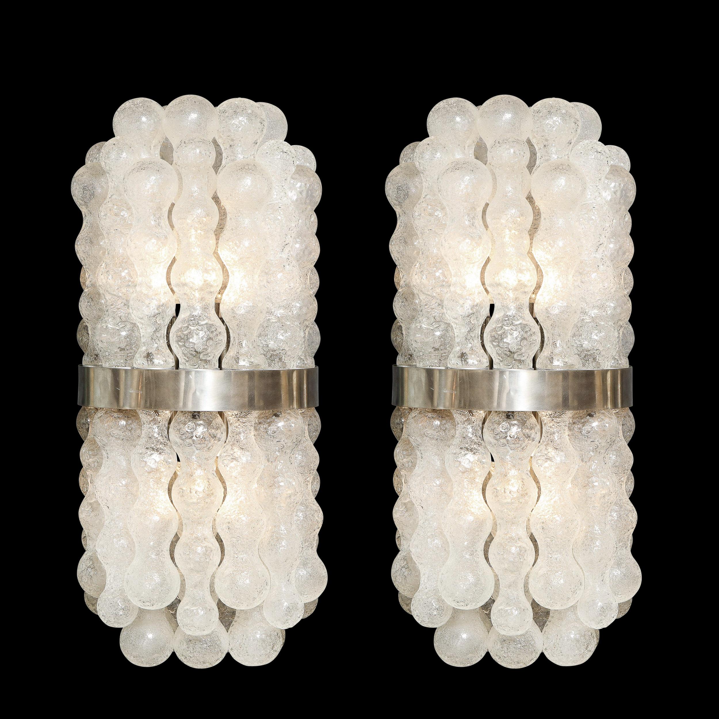 This sophisticated and stunning pair of Mid Century Modern sconces were realized in Murano, Italy- the island off the coast of Venice renowned for centuries for its superlative glass production. They feature bowed bodies composed of a wealth of