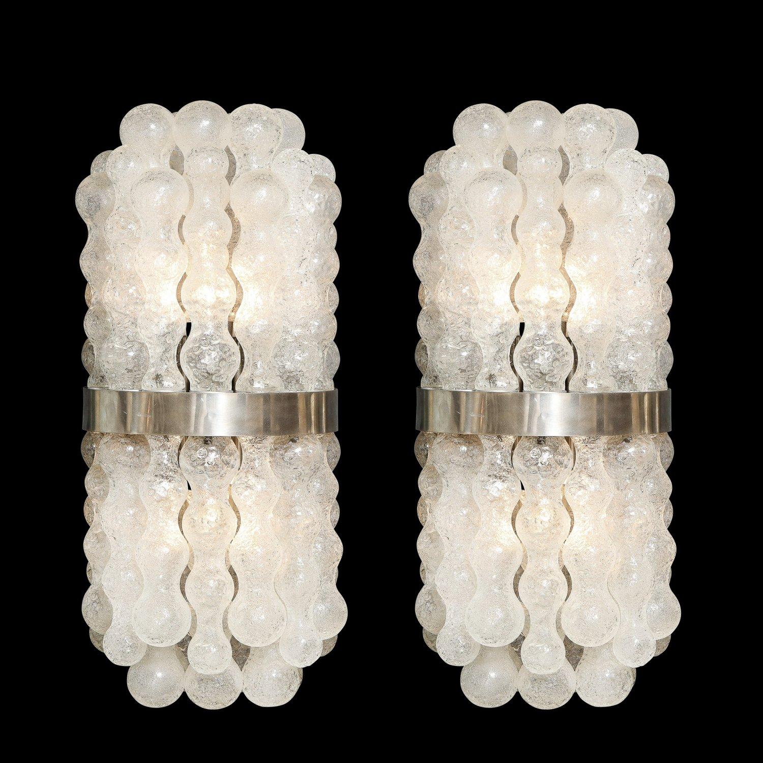 This sophisticated and stunning pair of Mid-Century Modern sconces were realized in Murano, Italy- the island off the coast of Venice renowned for centuries for its superlative glass production. They feature bowed bodies composed of a wealth of